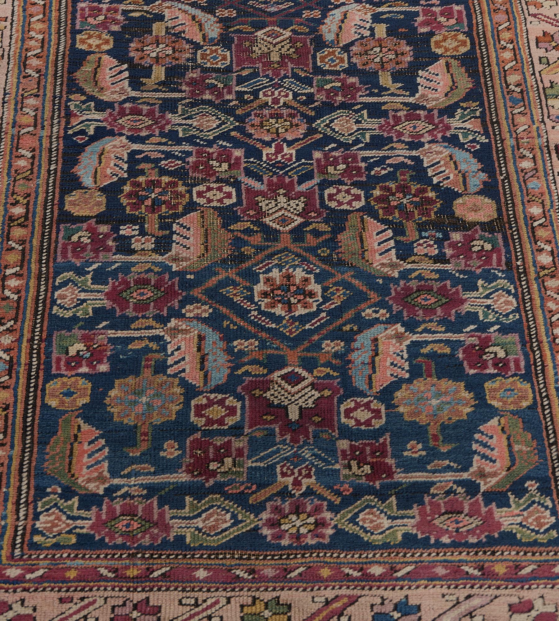 Ce chemin de table antique du Karabagh présente un champ bleu indigo avec un motif herati polychrome, dans une douce bordure rose terracotta de palmettes angulaires polychromes et de vigne feuillue entre des bandes de vigne florale brun renard et de