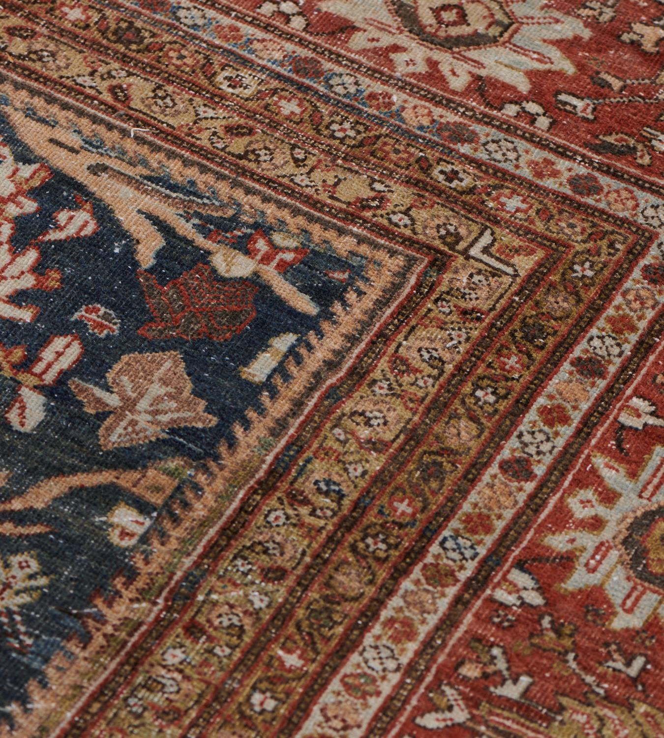 This antique, late 19th Century, Sultanabad rug has a shaded indigo-blue field with an overall design of ivory and soft apricot leafy and floral vine enclosing a floral spray surrounded by a garland of flowerheads, in brick-red border of polychrome