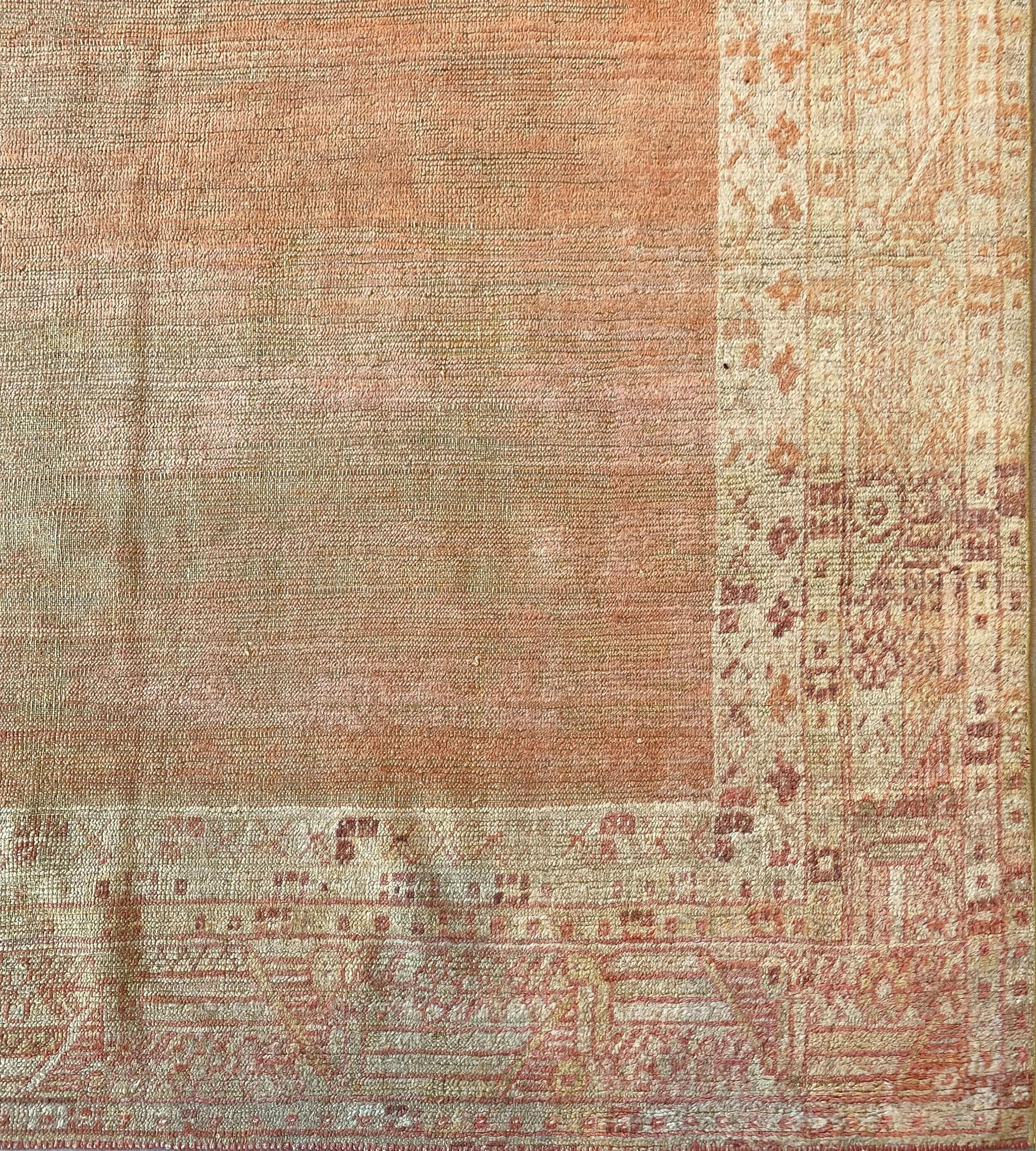 This antique Oushak rug has a plain shaded terracotta field, in a broad ivory border of terracotta and light brown linked panel floral vine between ivory narrow stripes containing flowerheads and angular floral vines.