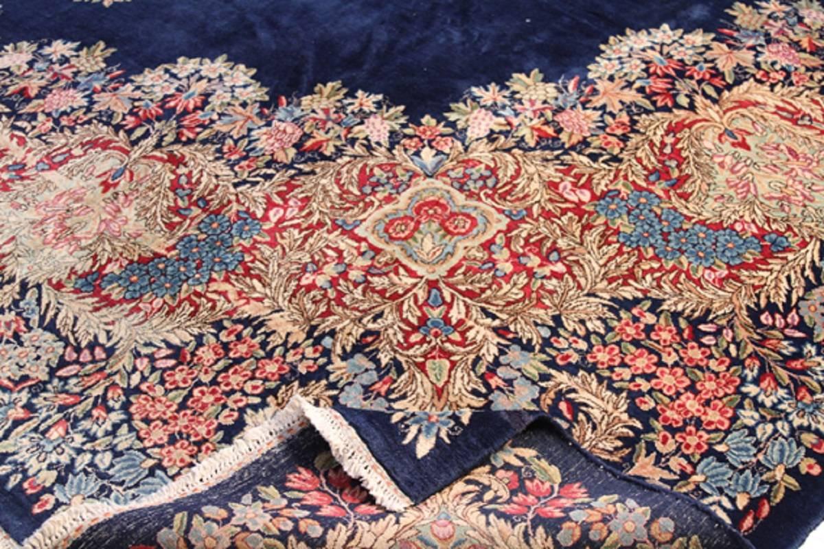 Handwoven old Persian Lavar Kerman design rug featuring a delicate oval-shaped floral medallion on a shaded royal blue field surrounded by a similar floral border in shades of raspberry, cornflower blue, pistachio, pale rose, sage and ivory. 