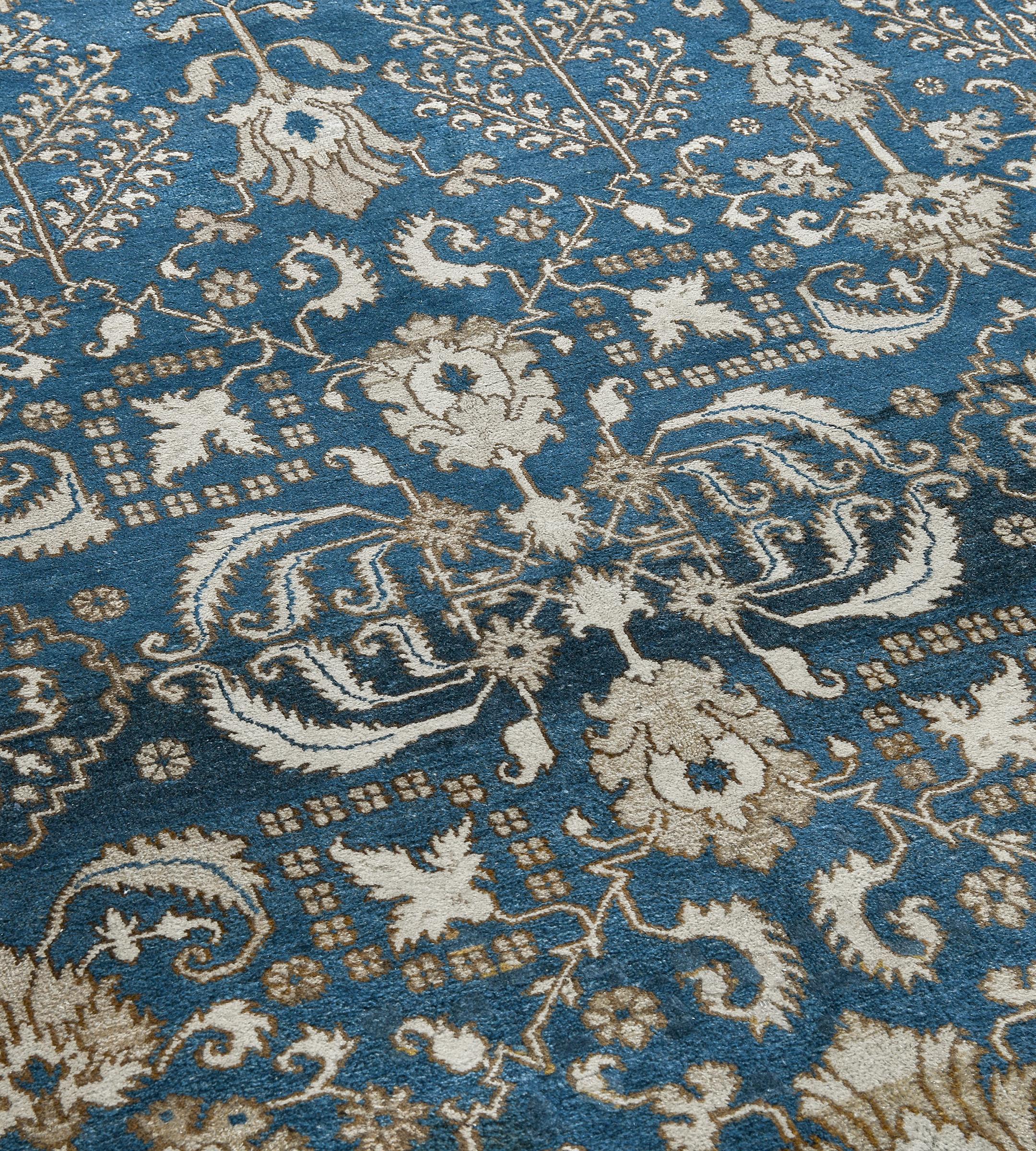 Questo antico tappeto indiano Agra ha un campo azzurro sfumato con un disegno generale di coppie di foglie seghettate color avorio, marrone bufalo e marrone caramello che collegano coppie di palmette affiancate da file verticali di palmette e tralci