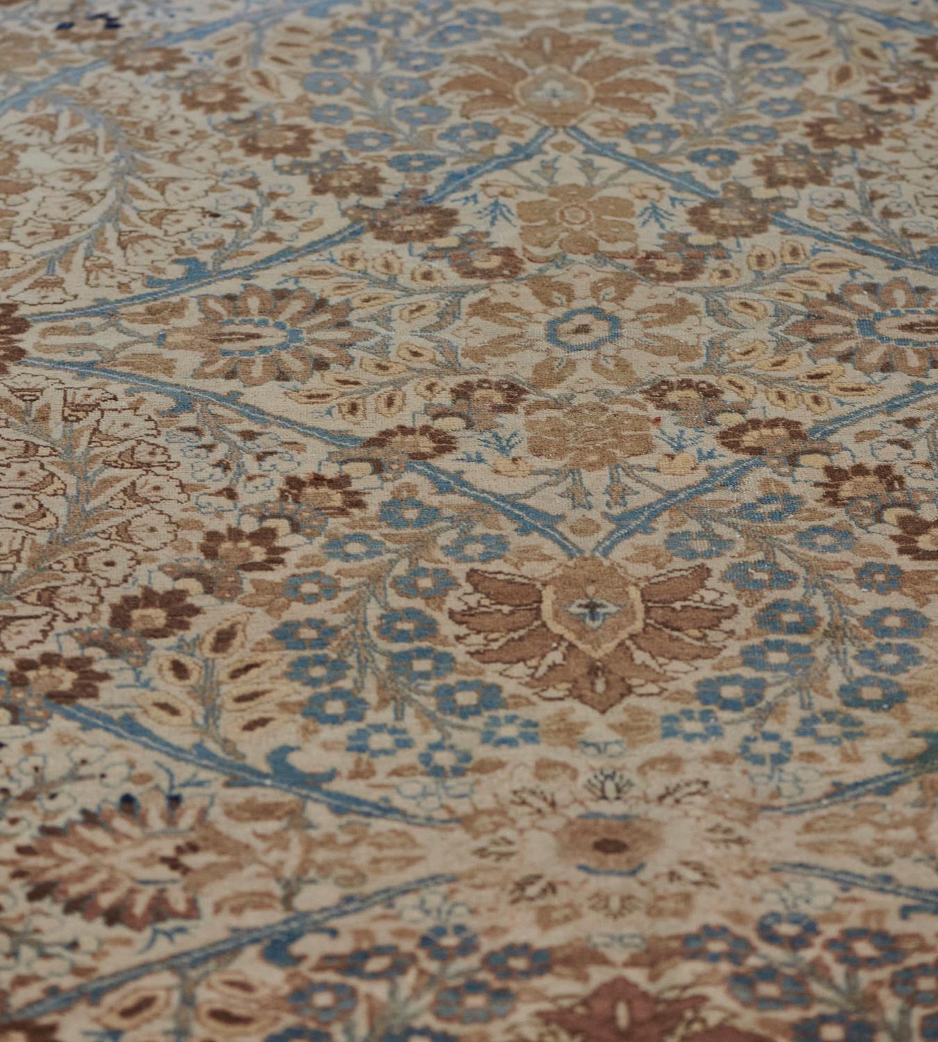 This antique Tabriz rug has a shaded ivory field with an overall design of mole-brown and light blue palmettes linked by horizontal light blue curved lattices forming a diamond lozenge enclosing a central palmette issuing delicate floral and