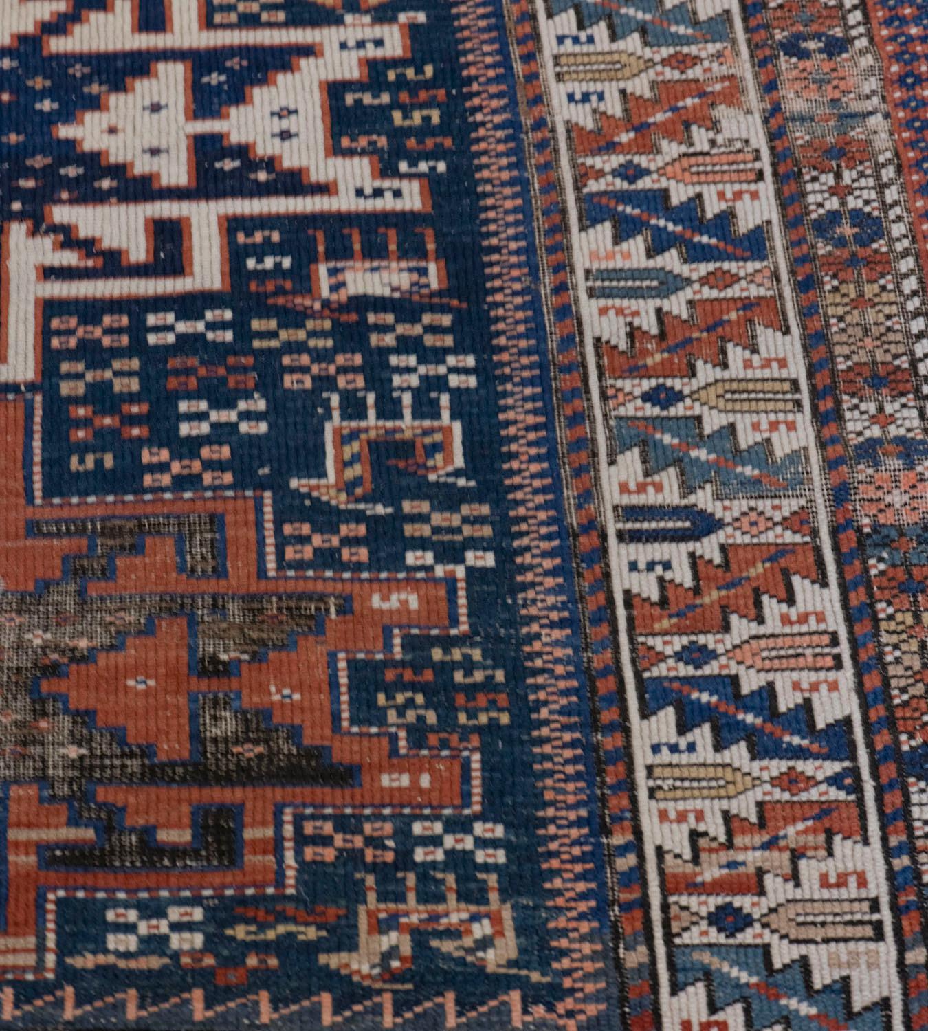 This antique Caucasian rug features a deep blue field scattered with polychrome S-motifs, stylized animals and polychrome angular floral motifs around with a column of three rust-red and ivory stepped, hooked and linked lozenges each containing a