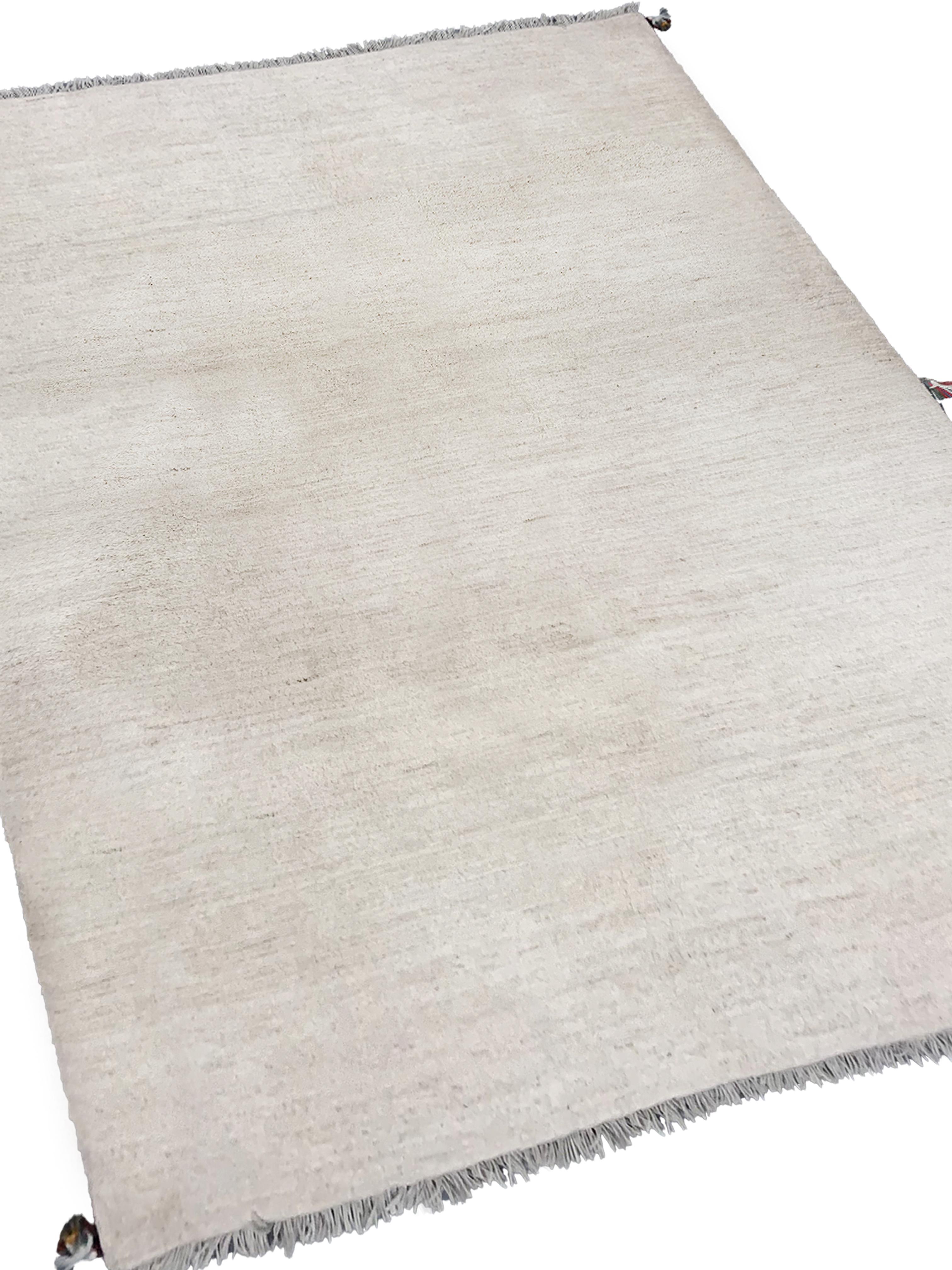 Dieser feine Wollteppich ist ein großartiges Beispiel für handgefertigte Gabbeh-Teppiche. Dieses moderne Stück ist schlicht und hat ein offenes Feld mit sechs Pompons an jeder Ecke und an den Mittelrändern. Dieses kühne Stück ist ein großartiges