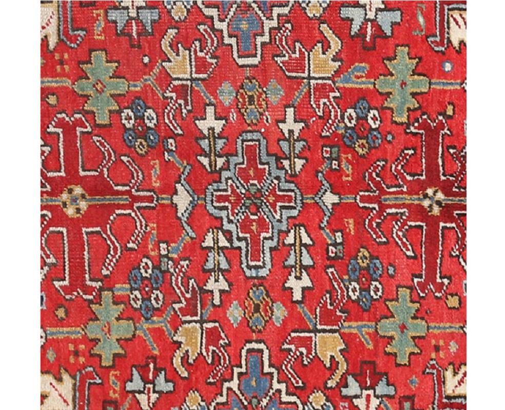 Handwoven old Persian Heriz rug with a red background and navy border, accented with shades of blue, ivory, green, and salmon. Iran.