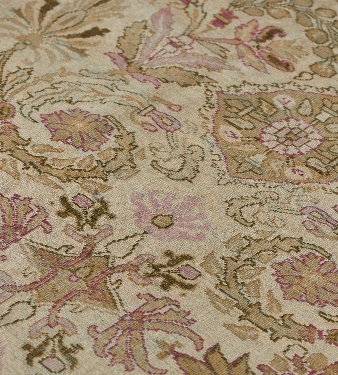 This Agra rug has an ivory field with an overall design horizontal bands of olive-green, golden-yellow and dusty-pink scrolling palmette and floral vines flanked by delicate floral sprays, in an olive-green border of meandering floral cartouches