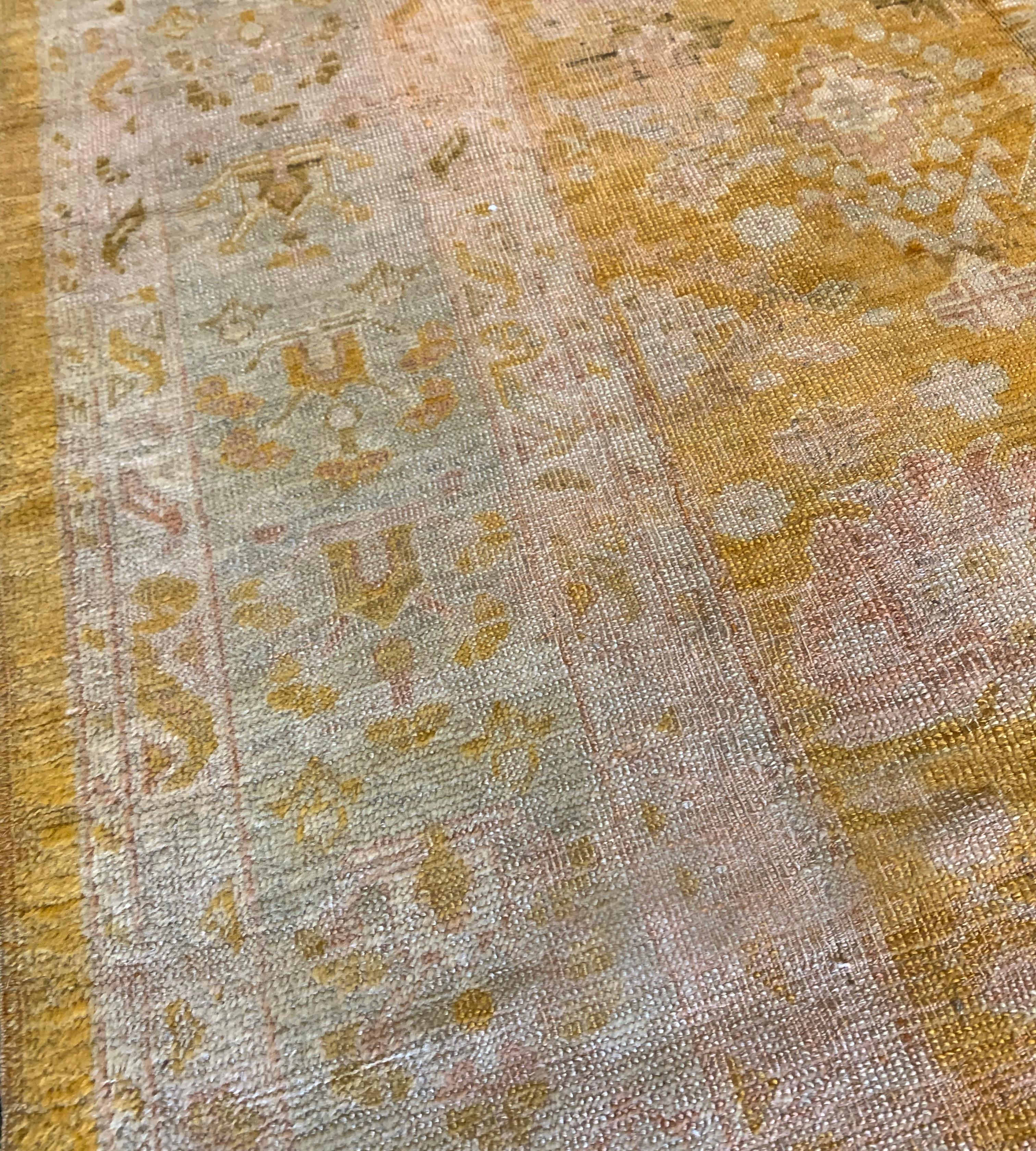 This antique Oushak rug has a lemon-yellow field scattered with ivory and dusty-pink palmettes, flowerheads and floral spays, in a broad soft-ivory and pale green border of golden-yellow and shaded brown floral vine between ivory narrow vine