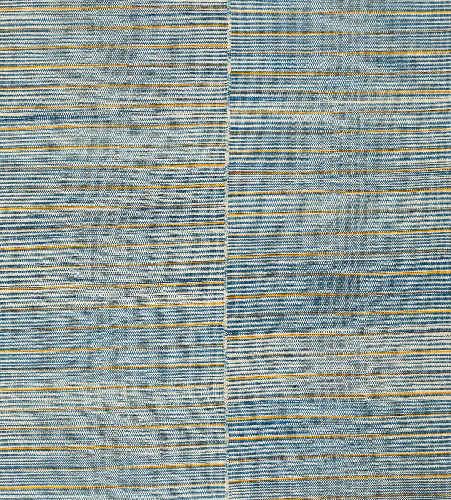 Esta alfombra plana tejida a mano es una interpretación contemporánea de la tradición kilim de Mazandaran, en suaves bandas lineales de azul cielo, arena, marfil y pizarra. Creada en Afganistán con lana hilada a mano y tintes naturales de origen