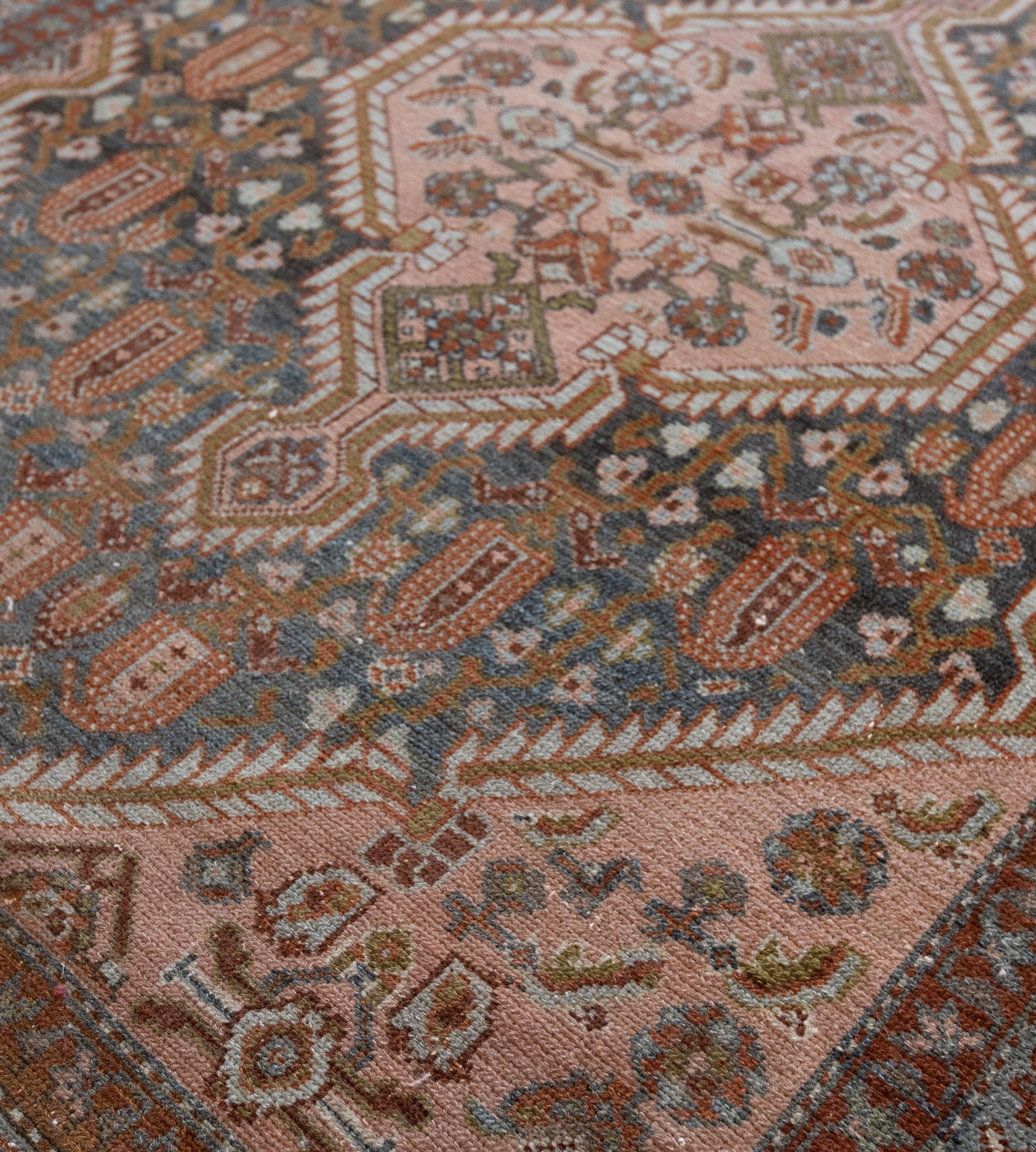 This Malayer rug has a shaded indigo field with a bold flowerhead and boteh vine around a central dusty-pink serrated lozenge with palmette pendants containing angular floral and serrated leaf vine, the dusty-pink spandrels with angular floral and