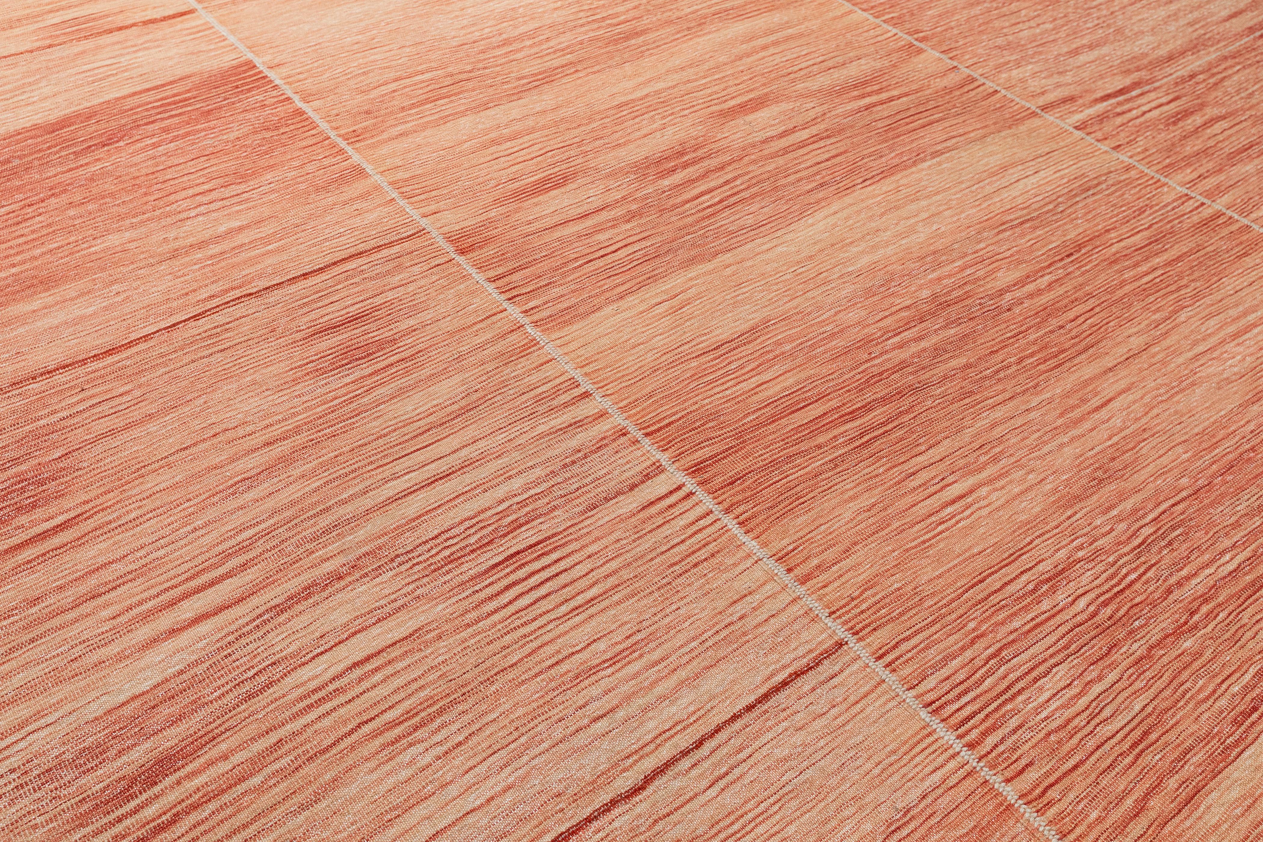 Eleva i tuoi interni con questo splendido tappeto Mazandaran a tessitura piatta, realizzato al 100% in lana filata a mano e tinto nei caldi toni del corallo. La tavolozza tonale minimalista e le bande orizzontali creano un sottile movimento sulla