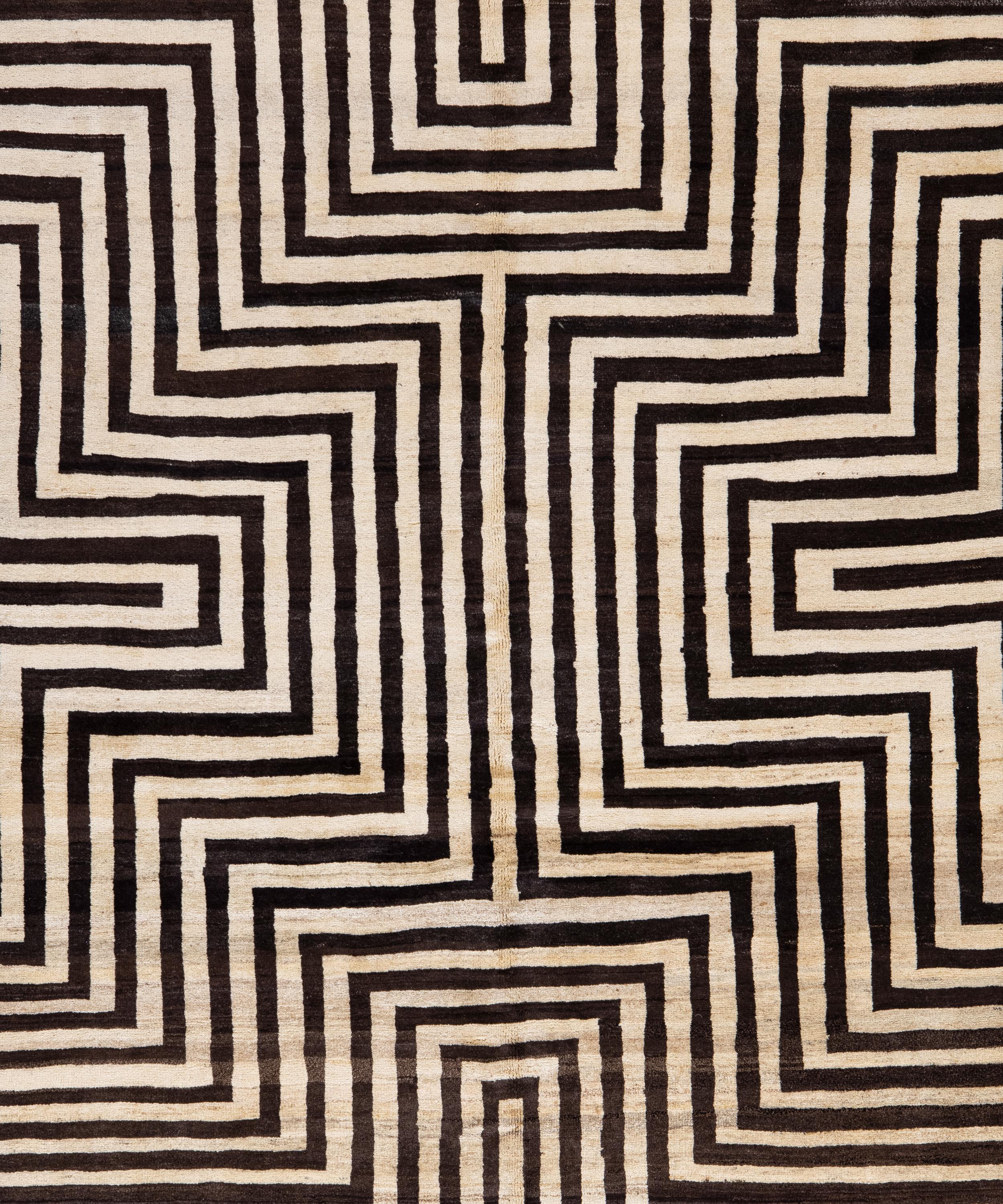 Audaz y arquitectónica, esta alfombra de lana tejida a mano presenta un llamativo motivo geométrico de inspiración laberíntica en negro intenso sobre un campo de marfil natural. Las líneas hipnóticas y la composición simétrica le confieren un