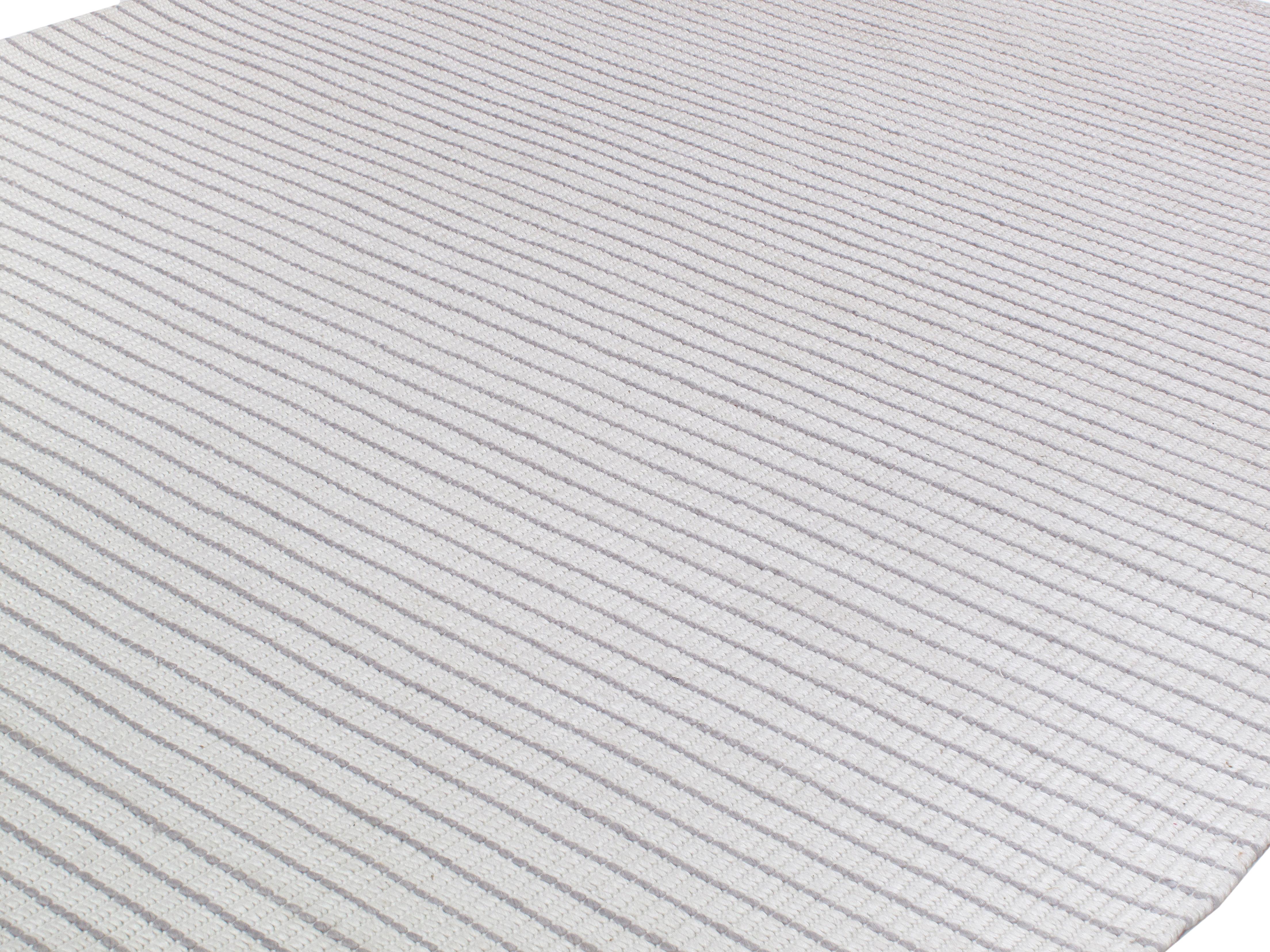 Dieser moderne Teppich wird in Indien aus hochwertiger neuseeländischer Merinowolle handgewebt, die wegen ihrer feinen Struktur und dauerhaften Qualität ausgewählt wurde. Die Palette besteht aus natürlich neutraler Wolle, die ohne synthetische