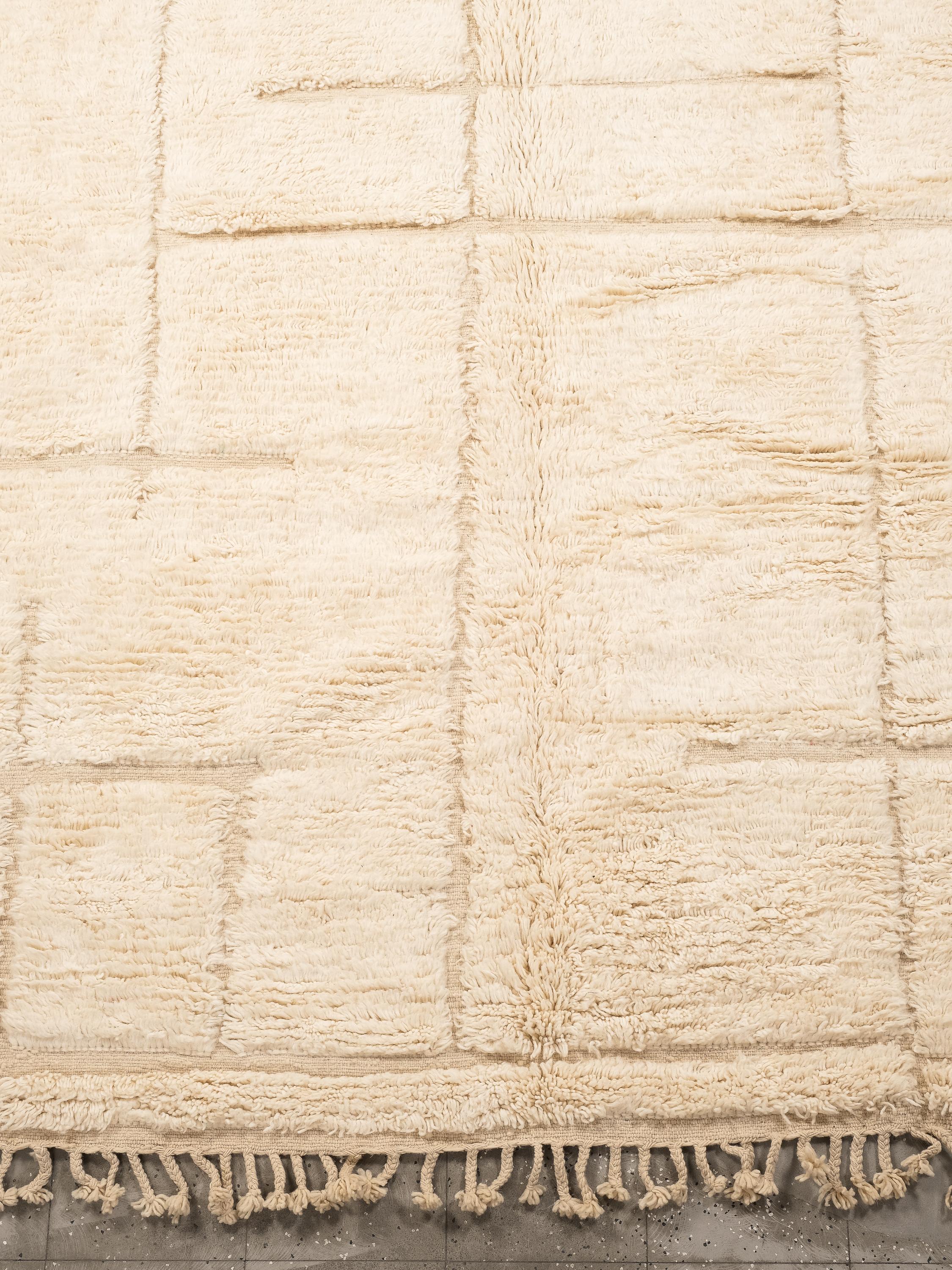 This handwoven Moroccan wool rug, measuring 303 x 224 cm, showcases the timeless artistry of Berber craftsmanship. Handwoven from 100% natural wool, the rug features a soft cream base adorned with a harmonious geometric pattern in muted tones. The