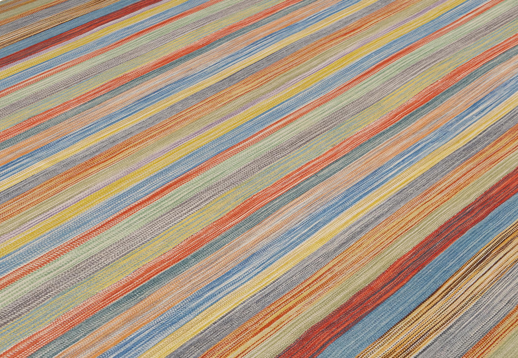 Esta vibrante alfombra plana tejida a mano presenta un colorido diseño de rayas verticales, inspirado en las técnicas de tejido tradicionales kurdas y reinterpretado por Nasiri Carpets para un público contemporáneo. El diseño combina tonos atrevidos