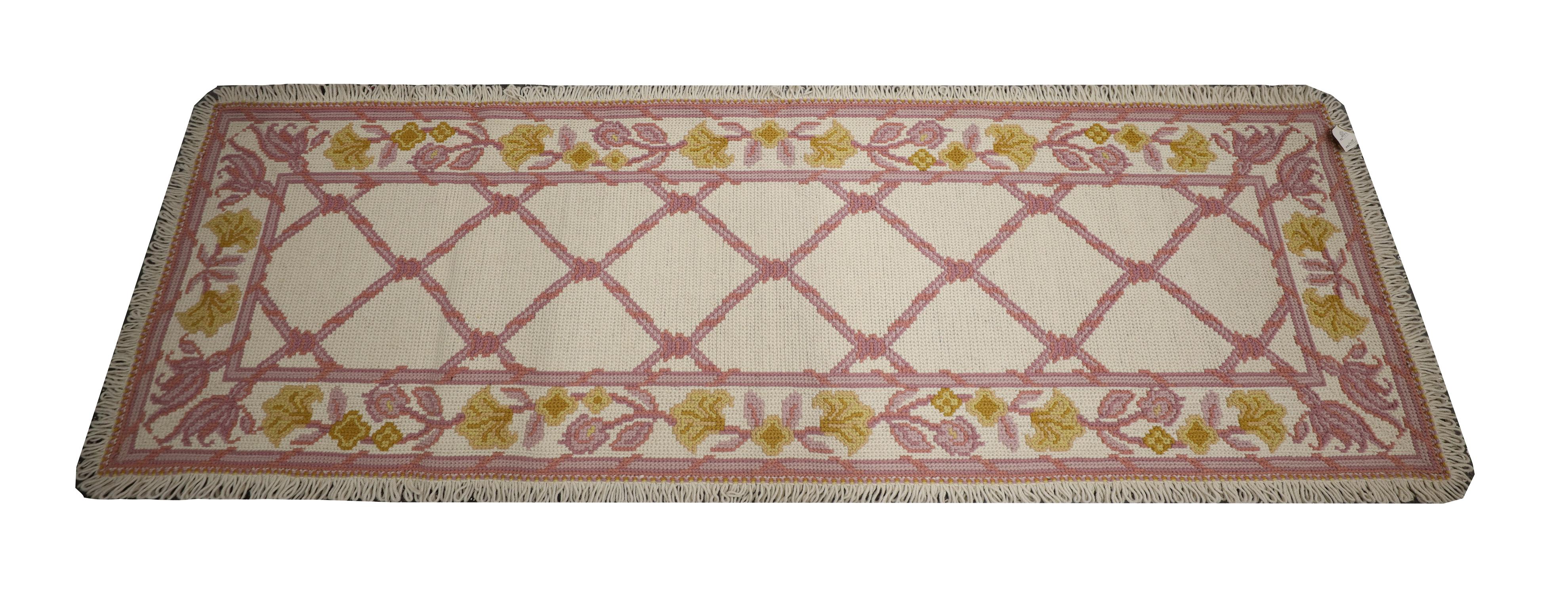 This fine wool needlepoint rug is a fine example of Portuguese rugs from the 20th century. The design features a symmetrical central design woven in pink and yellow accents on a subtle cream background. The edge of the rug has been finished with a