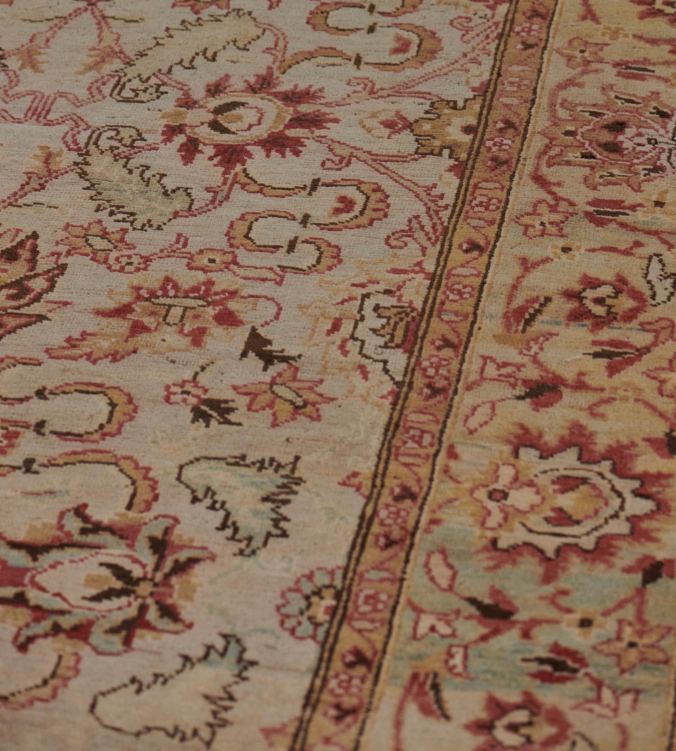 This Revival Agra rug has a shaded ivory-grey field with an overall design of shaded burgundy-red, apricot and light green palmettes and scrolling serrated leaf vine linking floral and further leafy motifs, in a light green-grey broad border of