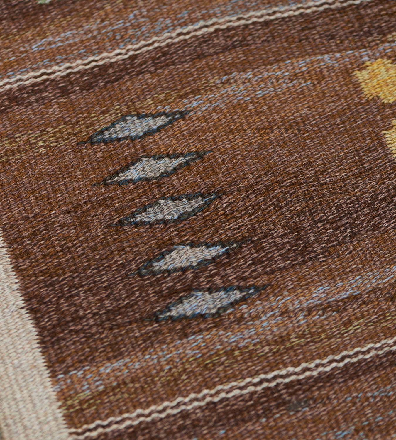 This mid-century handwoven Swedish flatweave Rölakan rug has a shaded caramel-brown field with seven broad horizontal panels each containing polychrome dice motifs and diamond lozenges around a large ivory I-shaped motif with a striped brown and