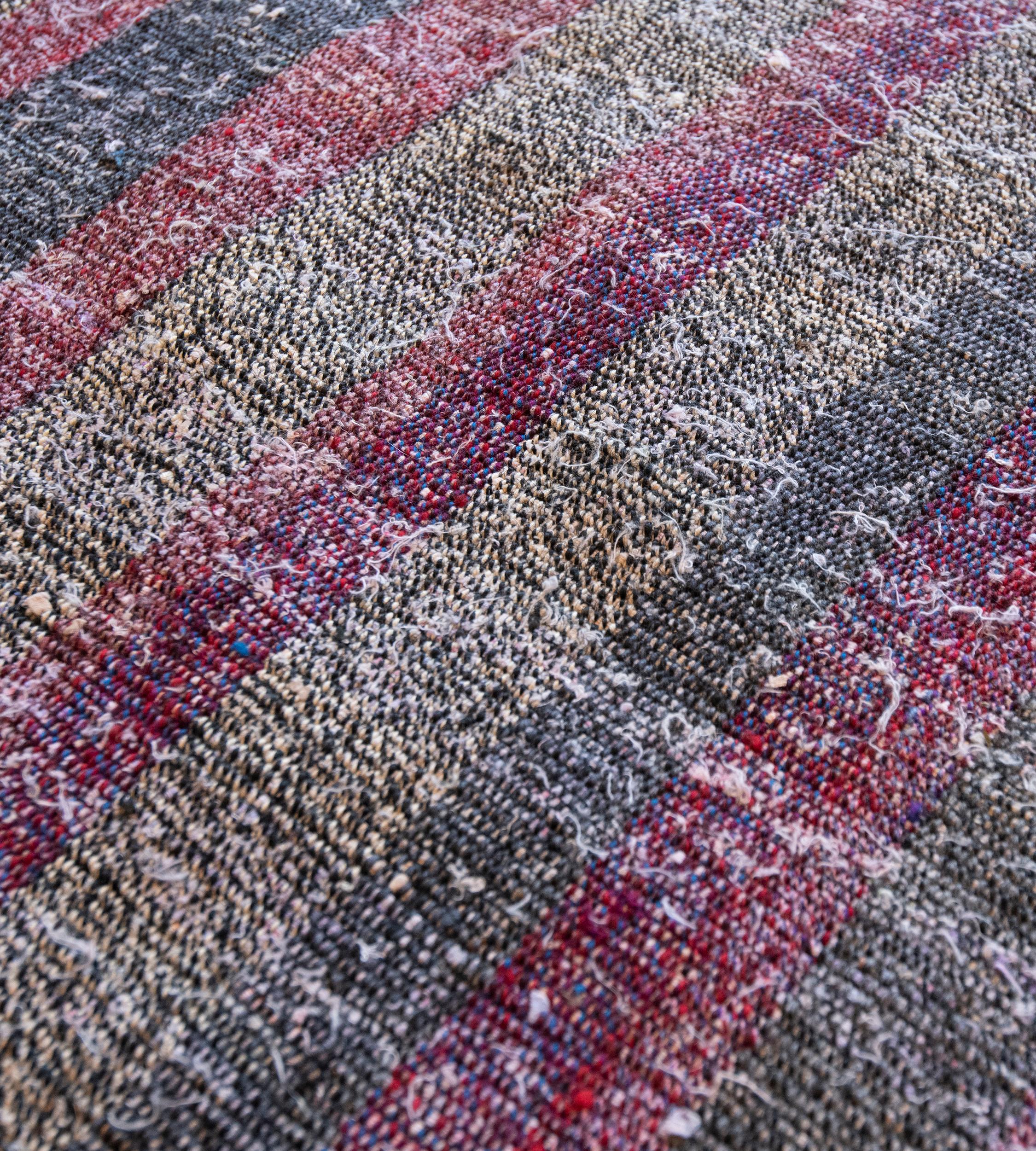 This handwoven flatweave Turkish carpet has a central field of vertical narrow bands of burgundy-red, steel-grey, shaded red and hazy-blue.