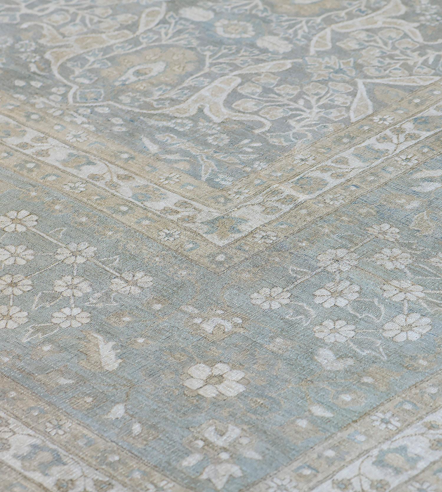 This Tabriz style rug features a shaded grey-blue field with an overall design of dense floral vine around double floral cartouches each containing a mole-grey palmette, in a broad shaded blue-grey border of alternating flowerhead sprays and floral