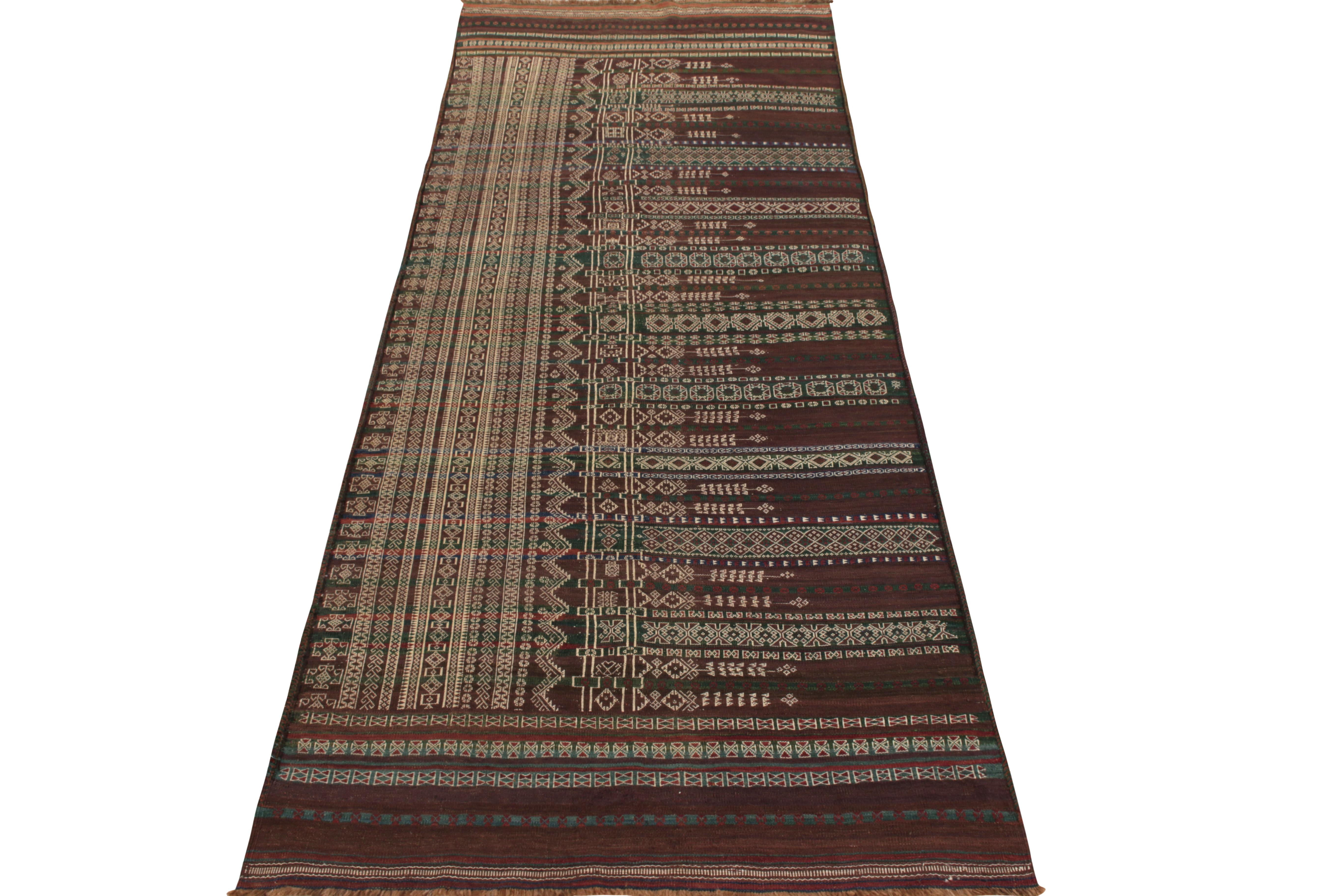 Hand woven in wool circa 1950-1960, a 4x11 vintage mid century Persian kilim rug from the Baluch lineage enjoying vibrant red, blue, and most notably green colors in such a muted, striped fashion playing fabulously with warm beige-brown hues;