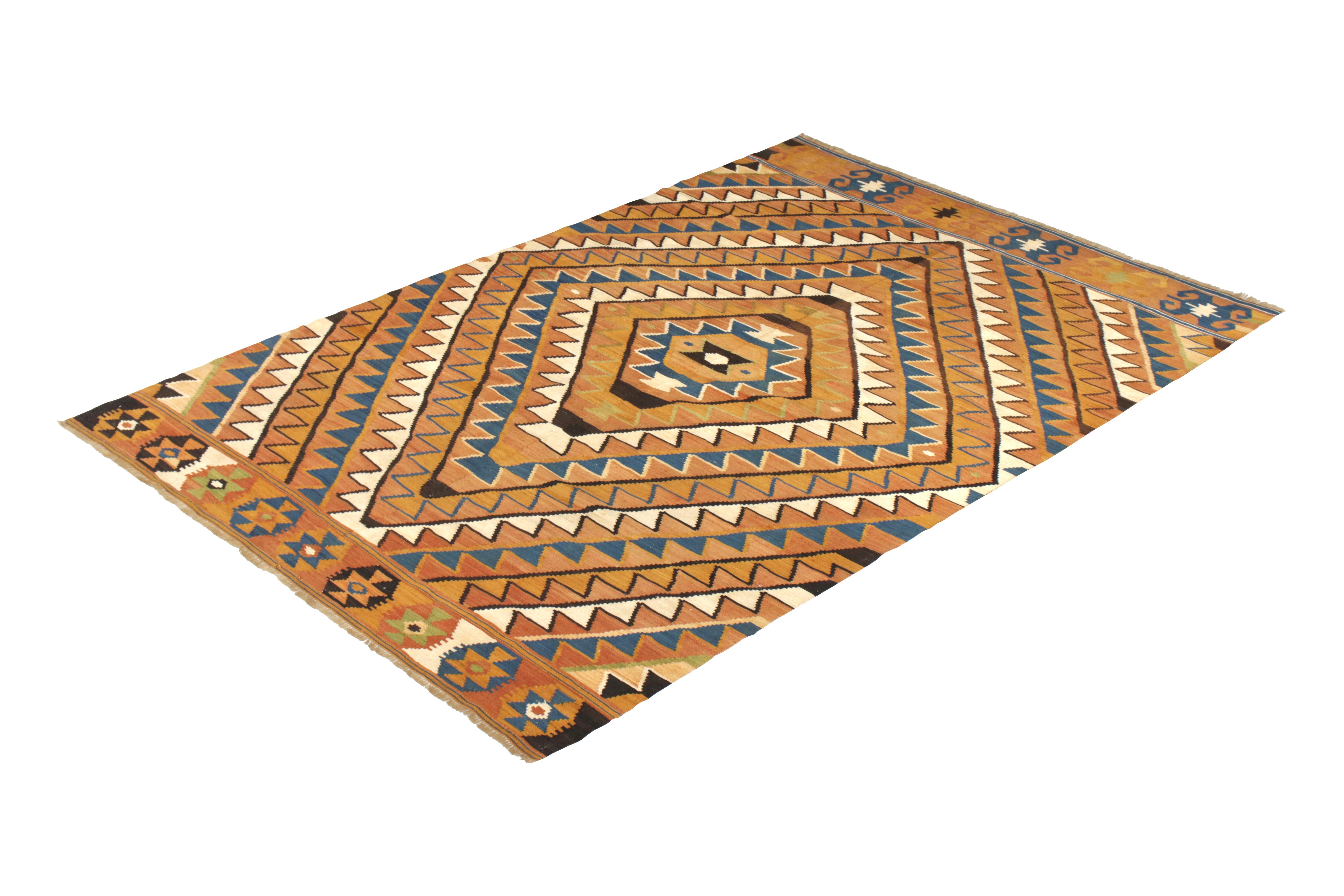 Handwoven in a wool flat-weave originating from Turkey circa 1950-1960, this vintage Kilim rug enjoys an uncommon play of rare colors, namely the prevailing gold and rust orange hues against blue and white in the all-over geometric pattern. Further