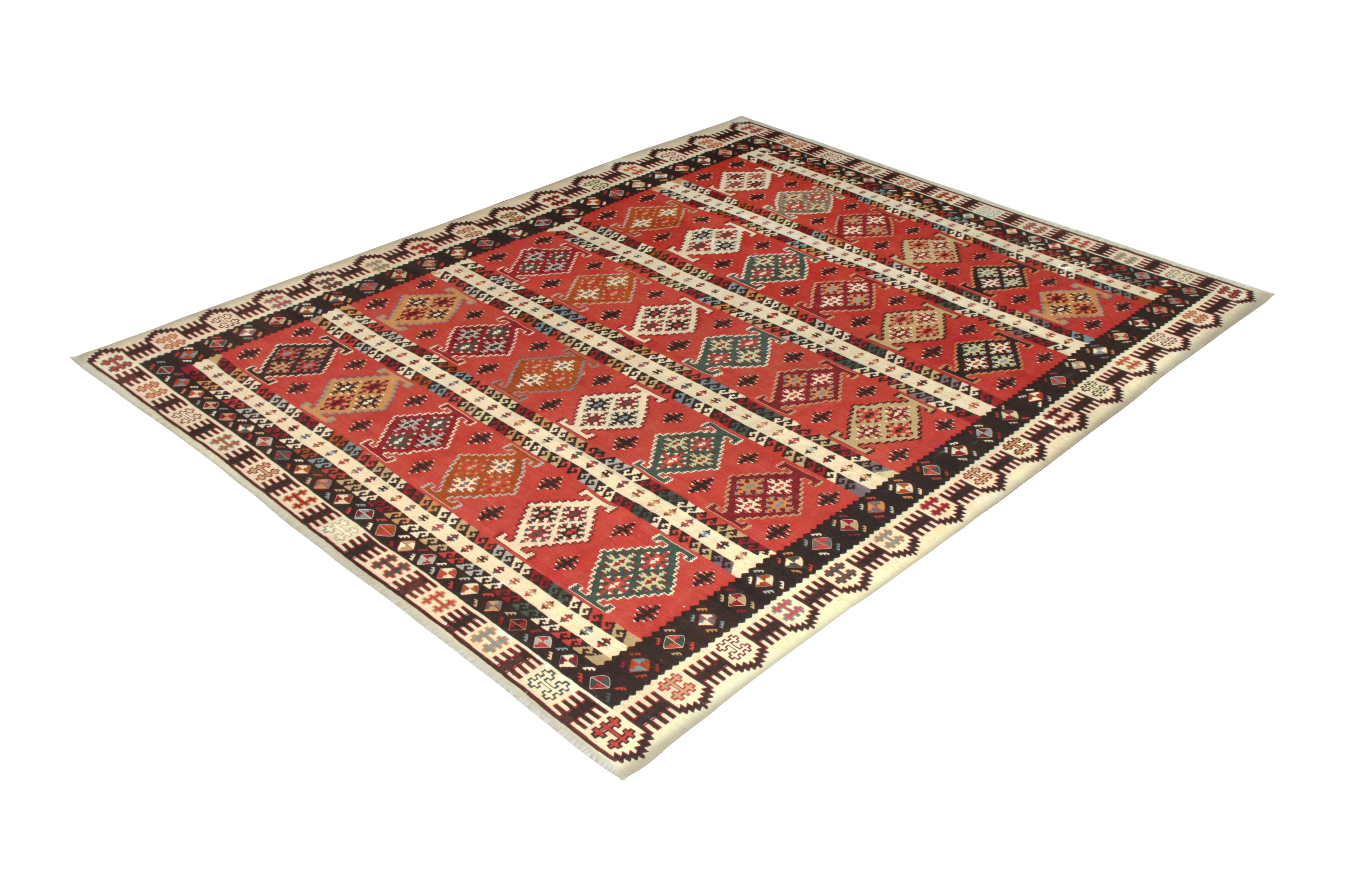 Handwoven in a wool flat-weave originating from Turkey circa 1950-1960, this vintage Kilim rug enjoys the culmination of spacious 9 x 11 size, a rich play of red and beige-brown tribal colorways, and a regal approach to the geometric all-over