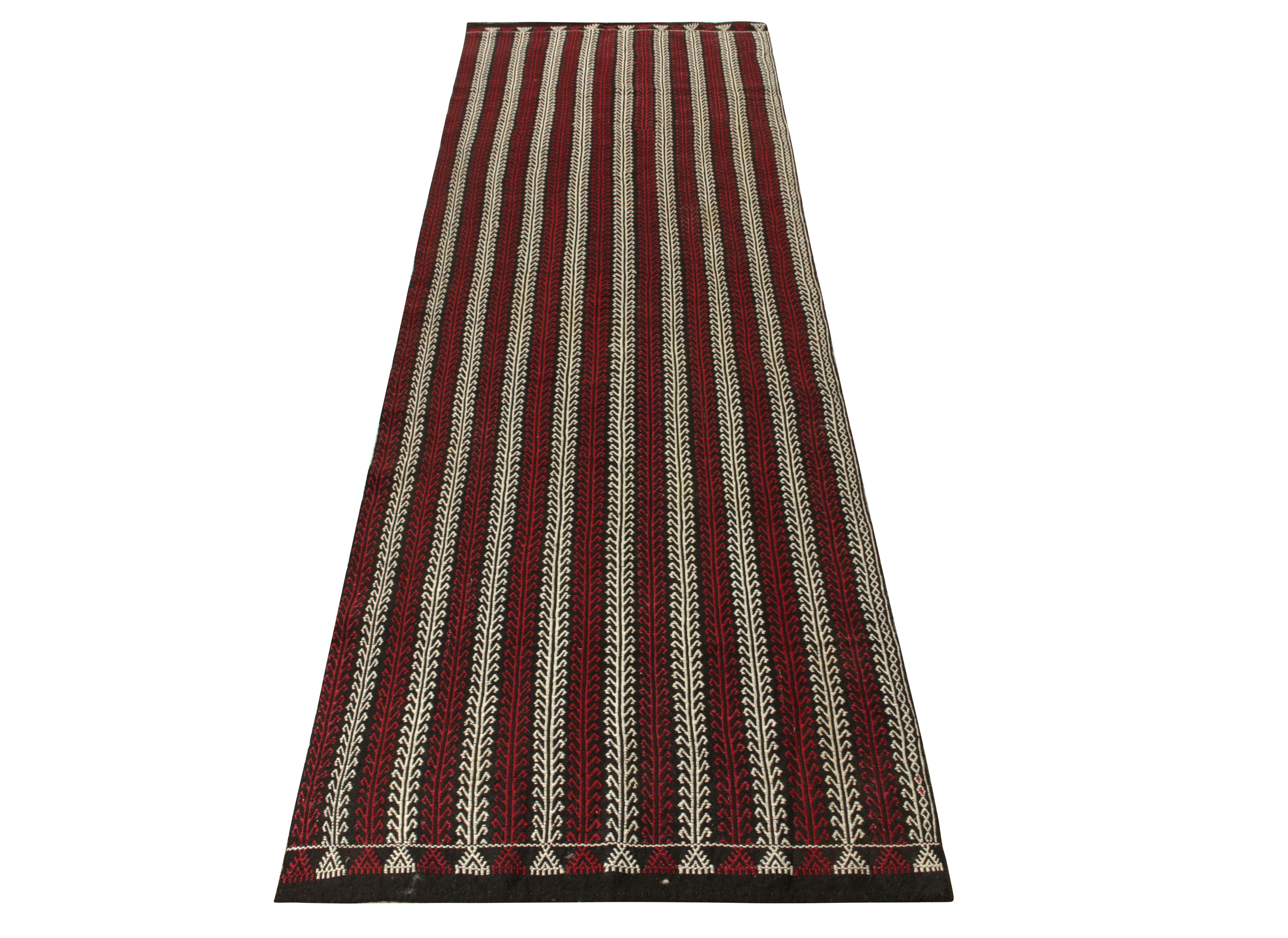Hailing from Turkey circa 1920-1930, a mature vintage kilim runner enjoying a symmetric geometric pattern branching symmetrically for a strong sense of movement—highlighted with rich red and white on a charcoal black scale. Enigmatic yet elegant, a