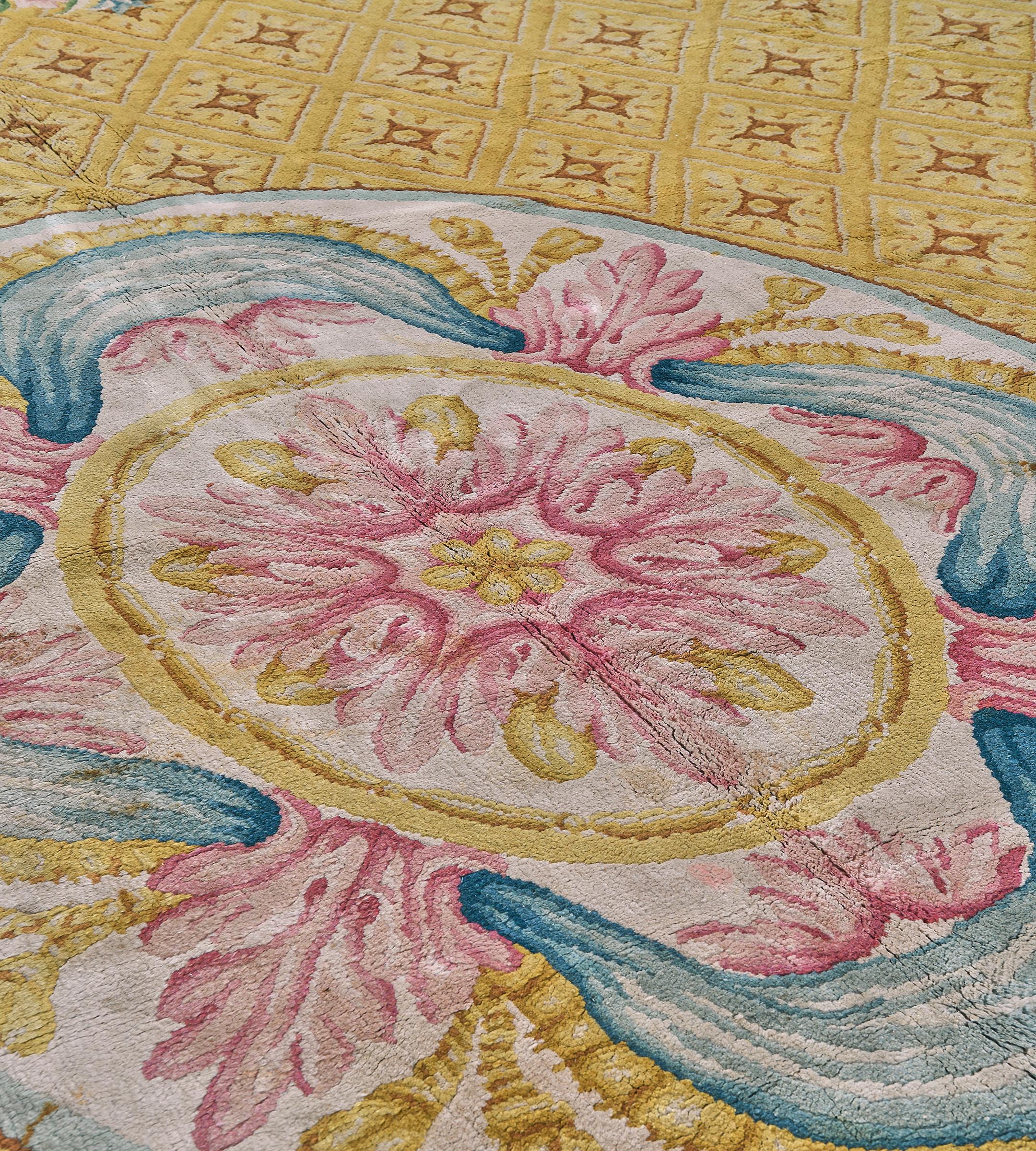 Ce tapis espagnol antique de la Savonnerie, datant d'environ 1900, présente un champ jaune d'or avec des rangées diagonales de panneaux contenant des motifs floraux centraux brun-renard et ivoire autour d'un grand ovale central ivoire avec une