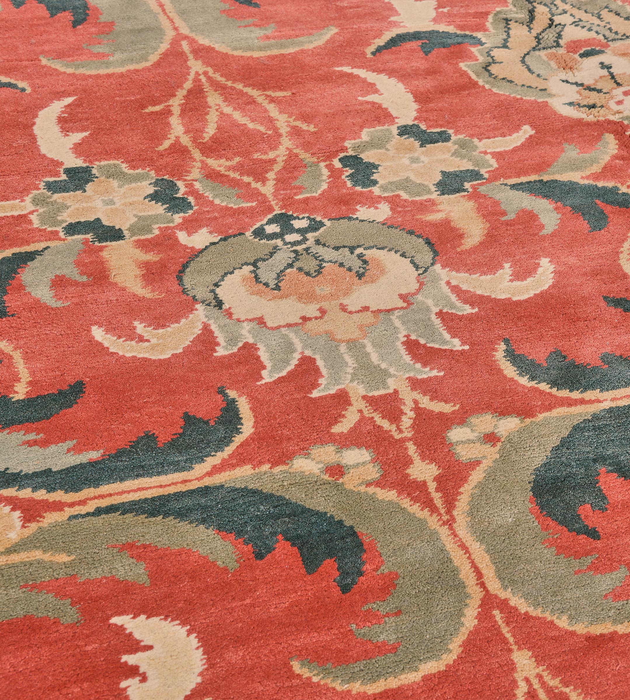 This traditional revival Arts and Crafts inspired rug has a shaded tomato-red field with an overall design of teal-blue and green-grey bold cusped acanthus leaves enclosing a green-grey, sandy-yellow and pale blue palmette linked by delicate leafy