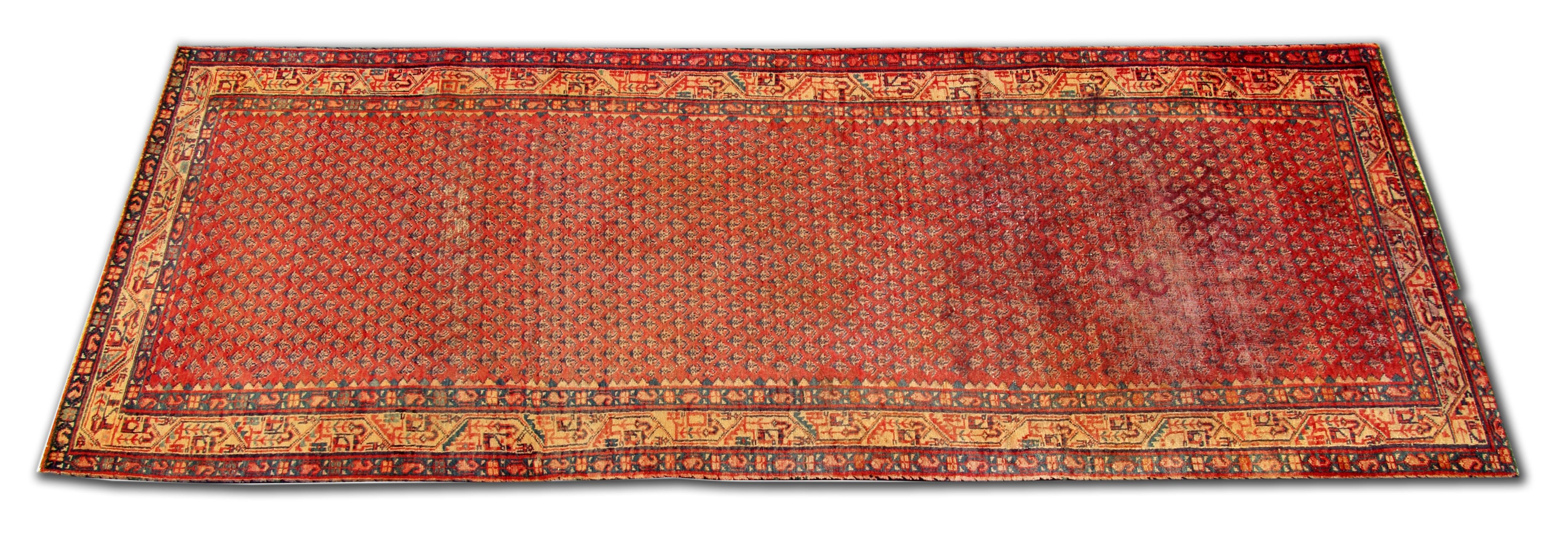 This fine red wool runner rug was woven by hand in the late 20th century and features a traditional repeating pattern central design, woven in accents of blue and beige on deep red background. This has then been framed by a layered border that