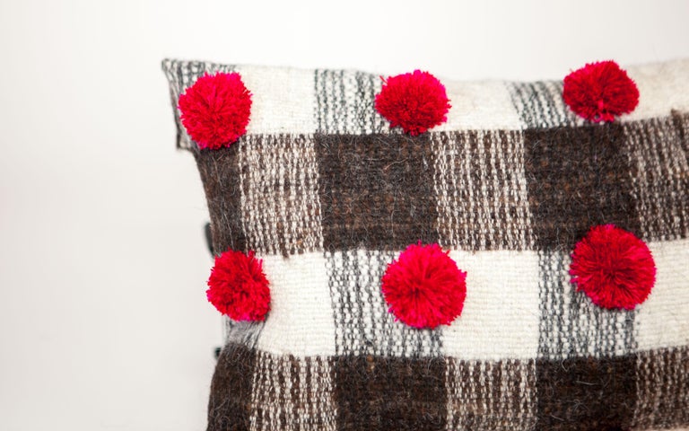 Woven on backstrap looms in Chamula, Chiapas, the textile of this delightful pillow is made 100% from wool sheared from Chamula community sheep, considered sacred in local culture, and dotted with deep red pom poms dyed with cochineal which is an