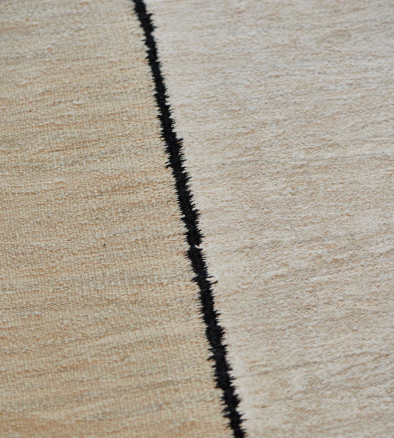 Ce tapis plat tissé à la main présente un champ principal composé de cinq larges bandes verticales d'un jaune sable et d'un ivoire nuancé, divisées par une étroite bande brun chocolat. 100% laine. État neuf.