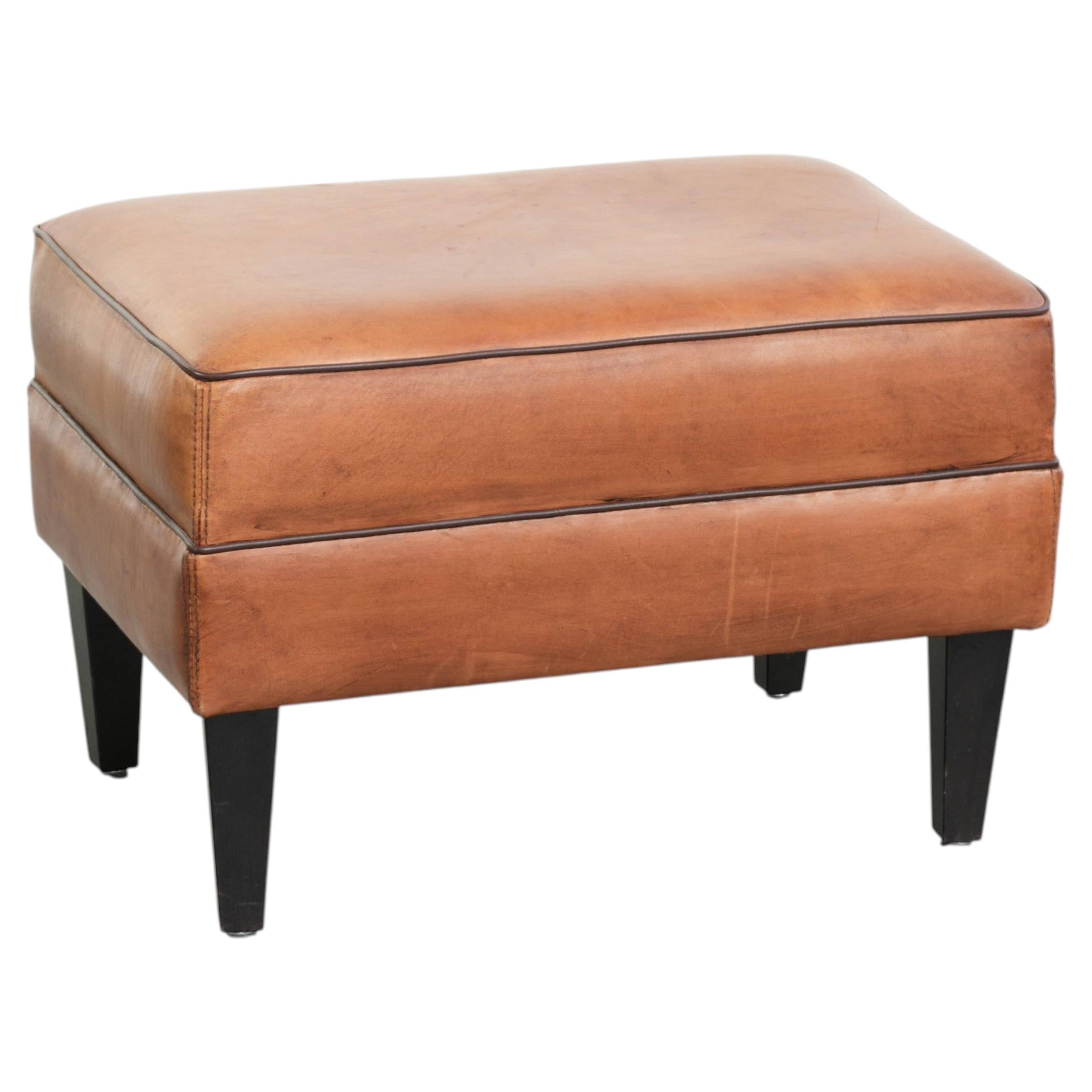 Handy sheepskin ottoman with warm colours finished with black piping
