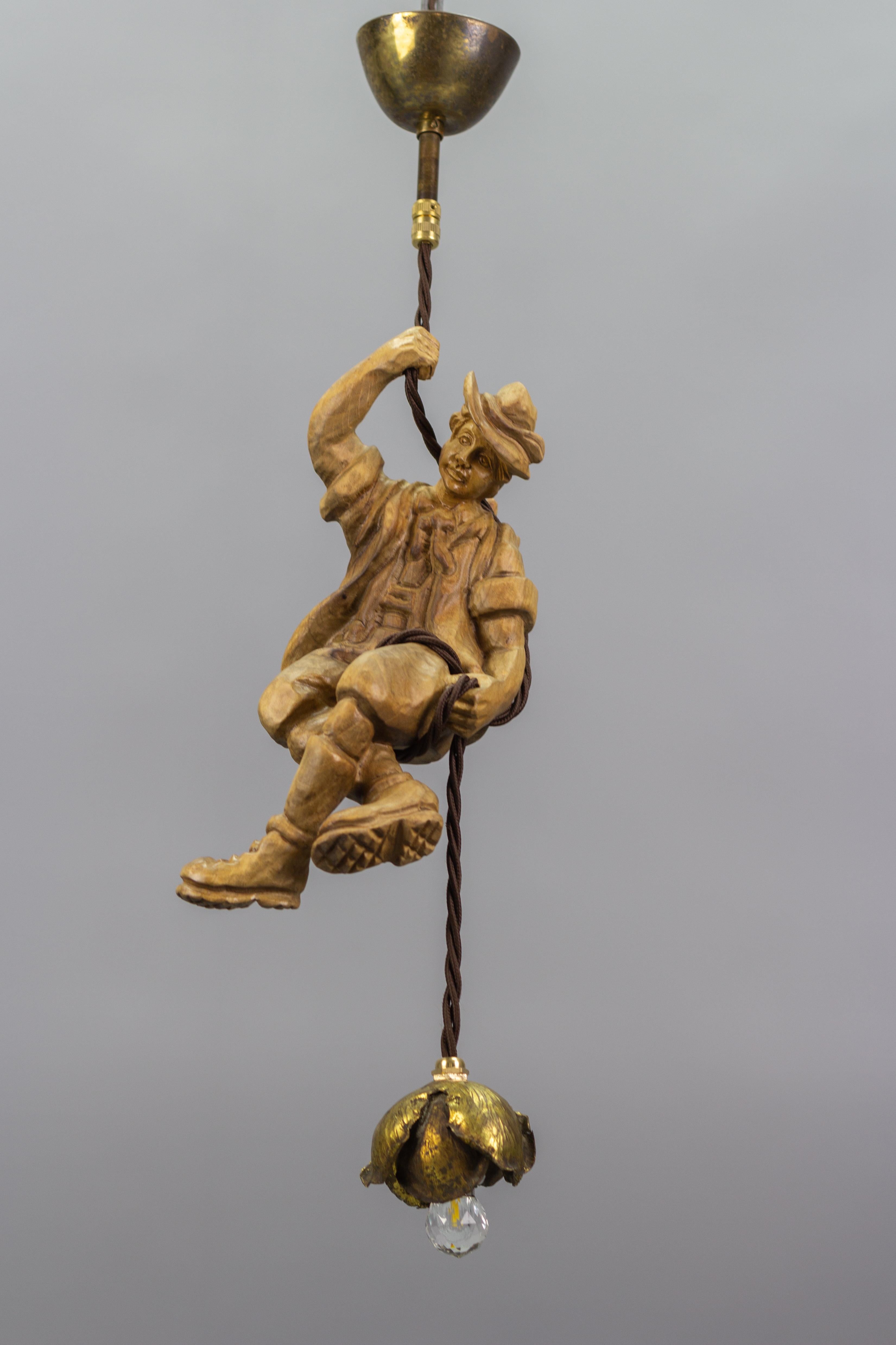 This wonderful German figural pendant lamp features a hand-carved figure of a mountain climber in natural brown wood tones. The detailed carved wooden mountaineer with a backpack is holding onto a rope and holding a flower-shaped brass lamp in one