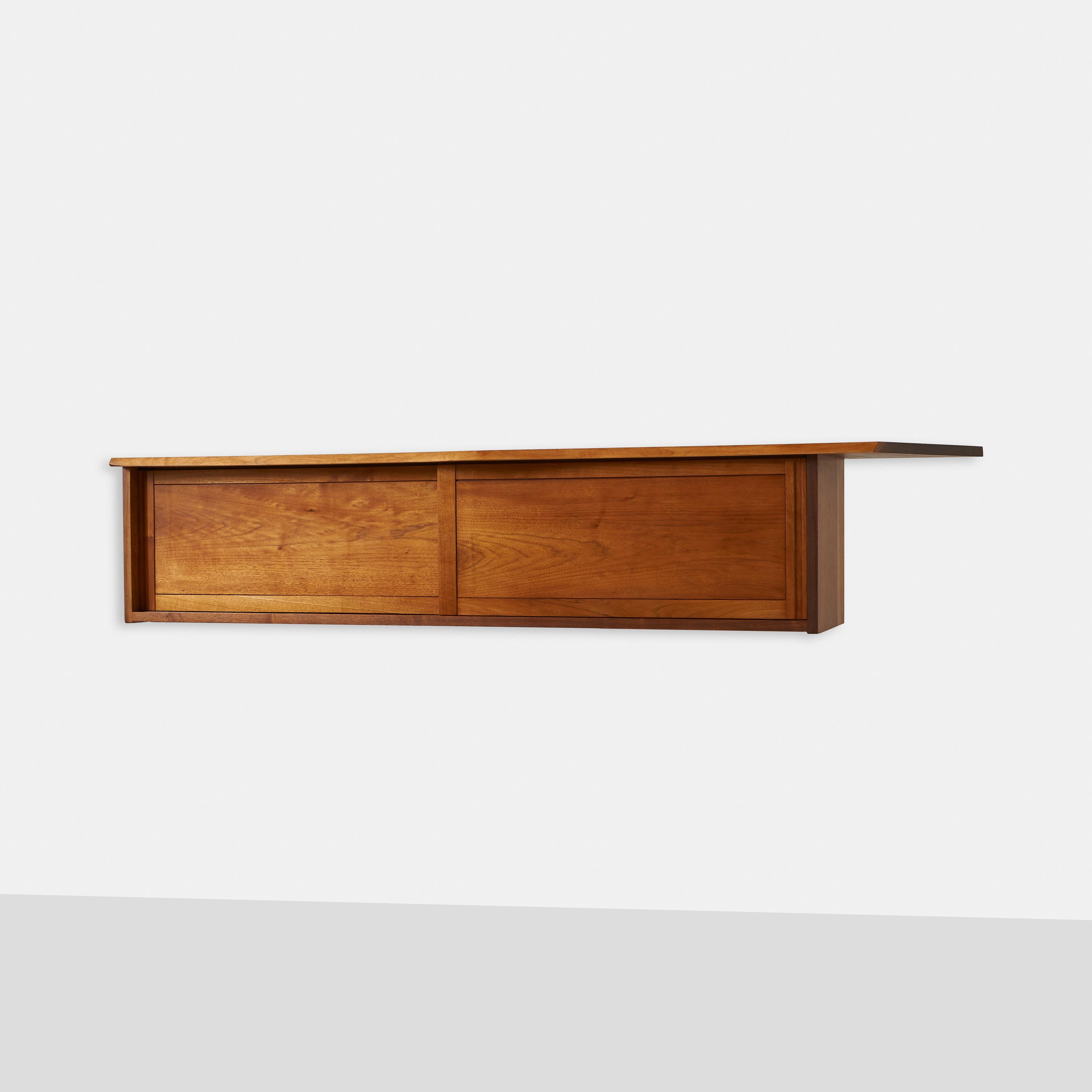 This rare and unique walnut hanging cabinet by George Nakashima is a beautiful and functional piece of modern furniture with sliding doors. The cabinet features an overhang top with one free edge above two doors that conceal one adjustable shelf.