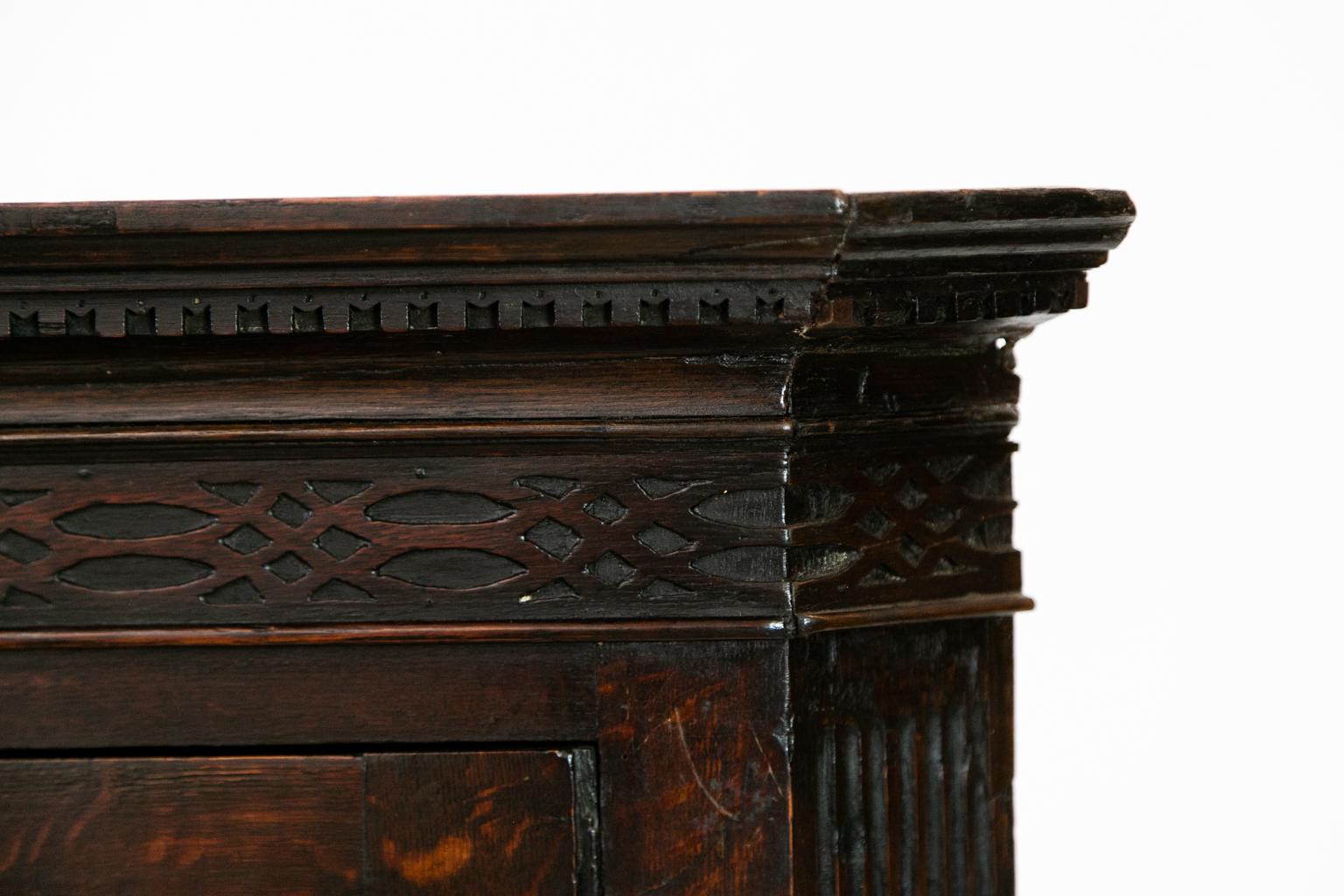 This hanging English oak corner cupboard has the original brass open fretwork escutcheon. The door has applied molding forming a center panel. The crown molding has carved dentil work and the base has shaped applied molding. The front exposes