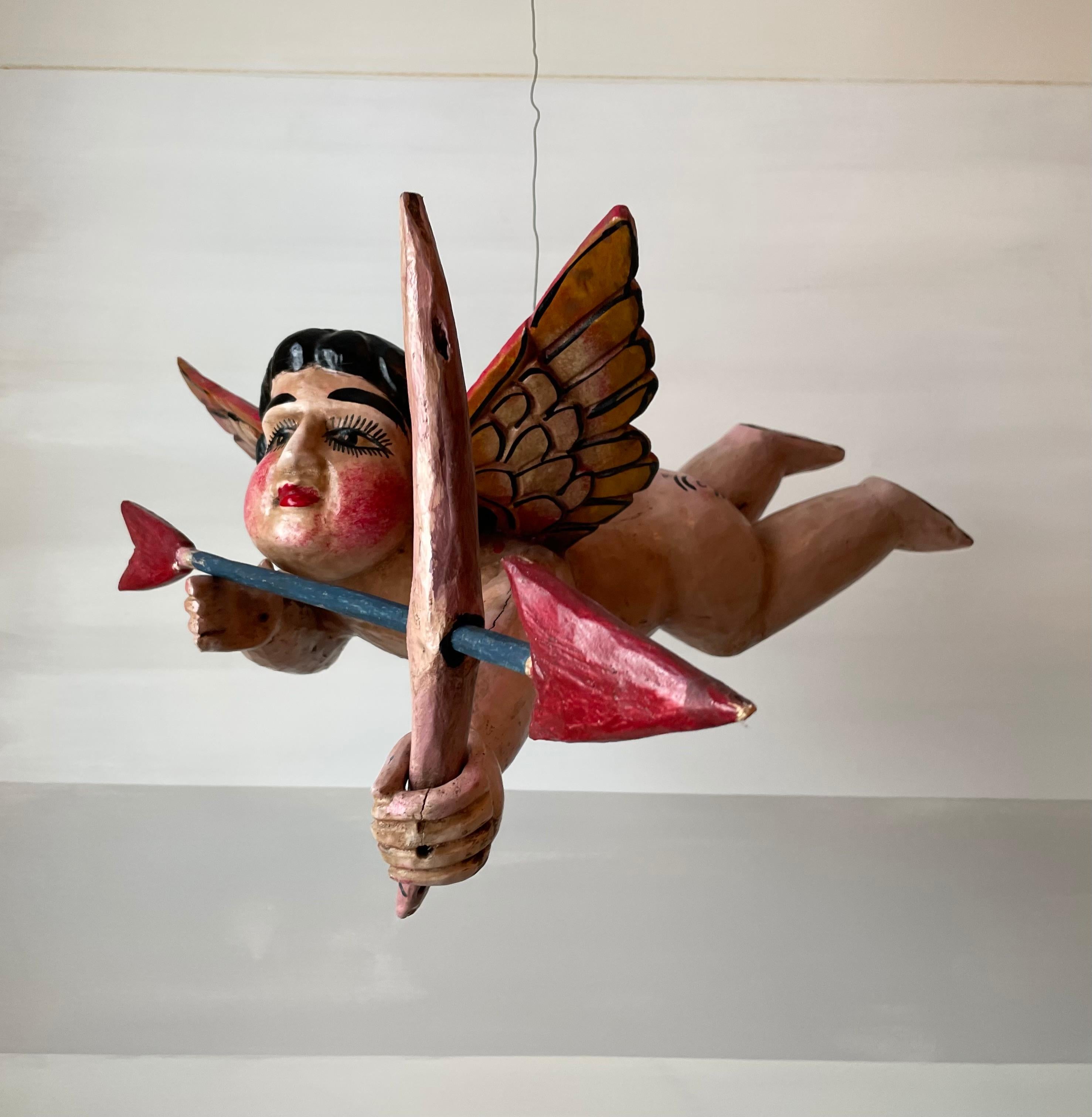 A rosy-cheeked wooden cupid to bring love into your life. This is a unique, hand-carved, hand-painted wooden cupid with a wire suspension and removable wooden bow and arrow. 

At 25