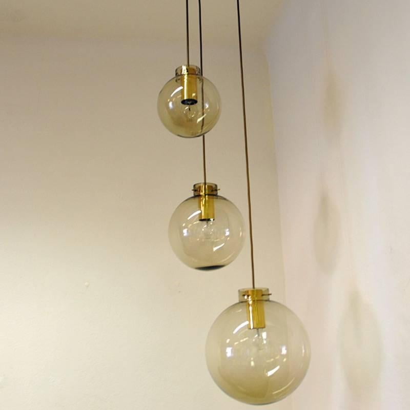Very special three domed pendant lamp from Høvik, Norway with lightly smoked glass domes in three different sizes. The smallest dome is on the top and the largest dome on bottom. The smokey glass domes are hanging on a brass cylinder and all three