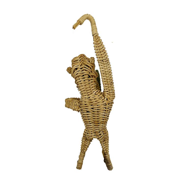 A small hanging wicker monkey holding a grouping of leaves. This cute brown monkey is created from wicker and features arms and legs which are bent so that they may hang from any spot. He has beaded eyes, a black face, and holds a bundle of green