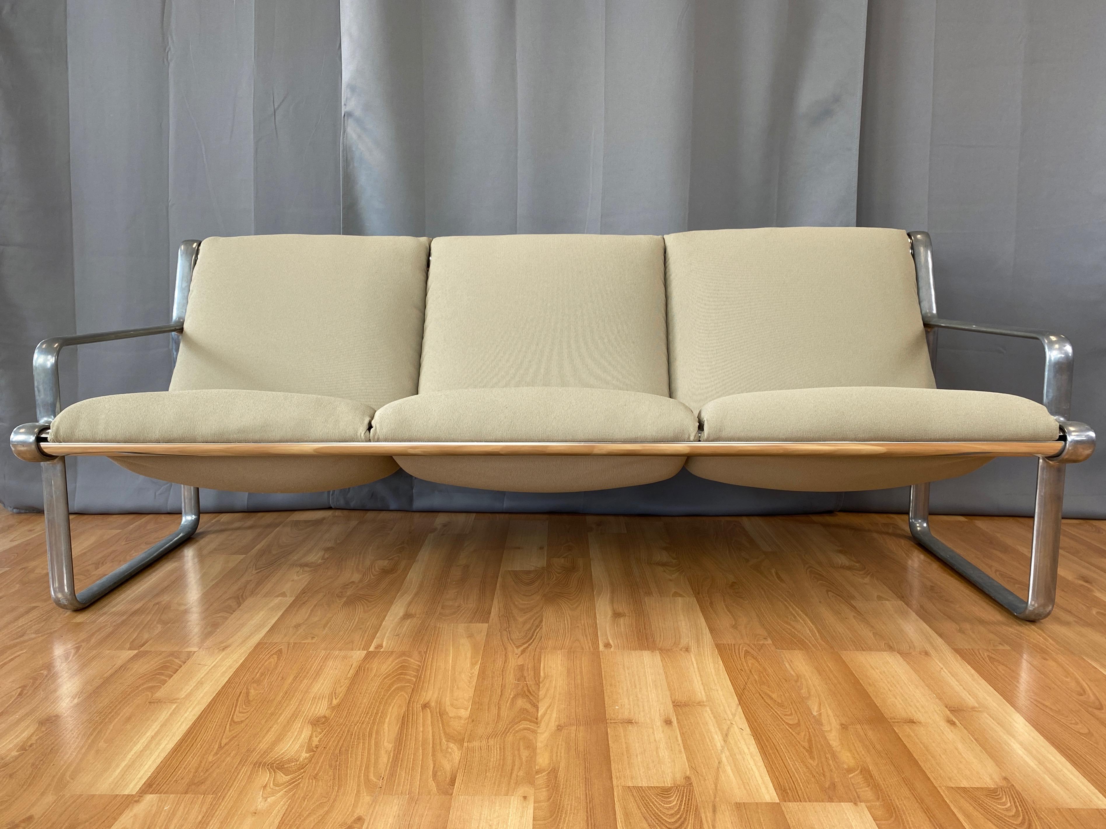 A very inviting and comfortable 1971 Knoll International aluminum three-seat sling sofa by Bruce Hannah & Andrew Morrison with new Maharam upholstery.

Minimalist and sleek cast aluminum frame with satin finish open arm sides connected by a pair of