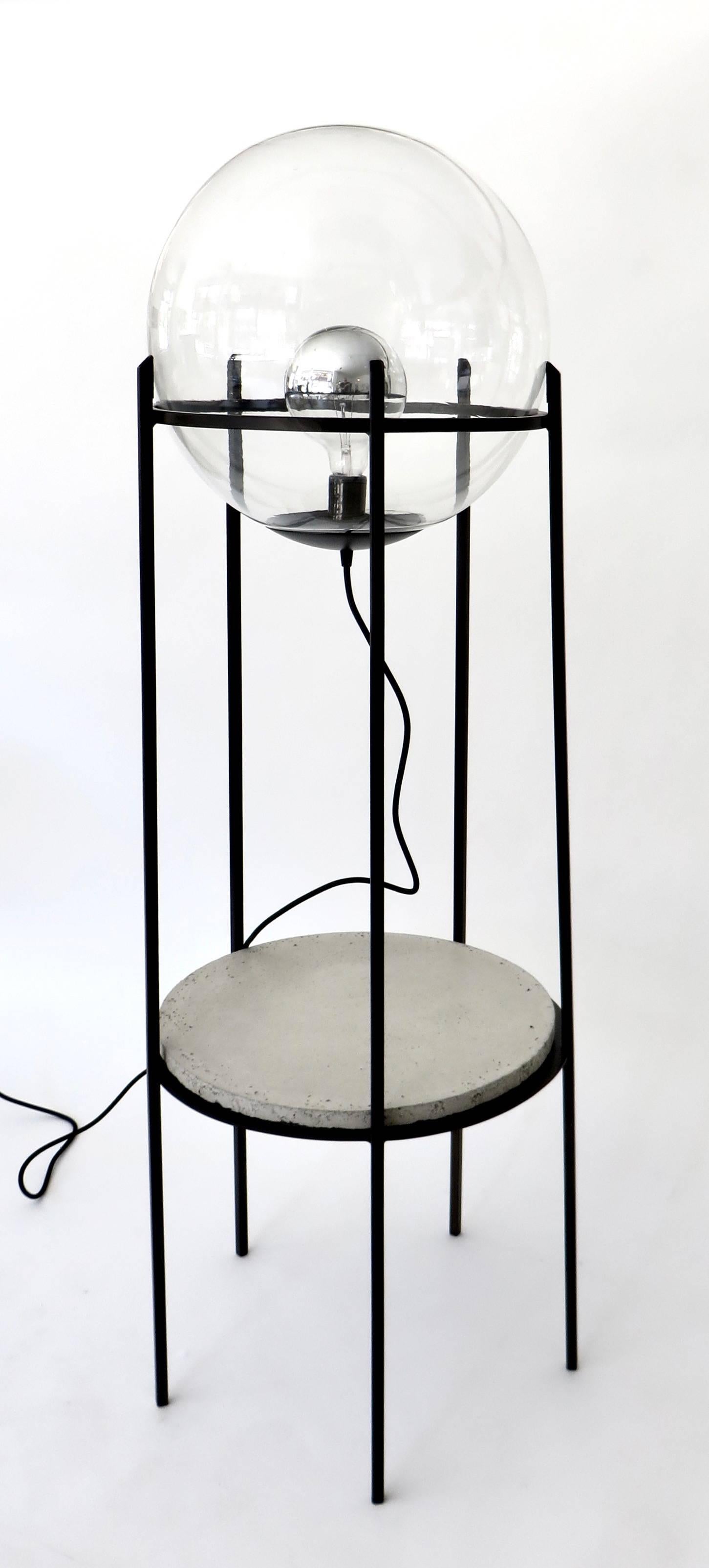 Two level lamp by contemporary artist and designer Hannah Vaughn.
Clear glass globe, cement plateau, and hand-wrought iron structure.
Edition of ten. This is #3 in the edition. 2016. Signed on underside of cement plateau

Hannah Vaughan was born