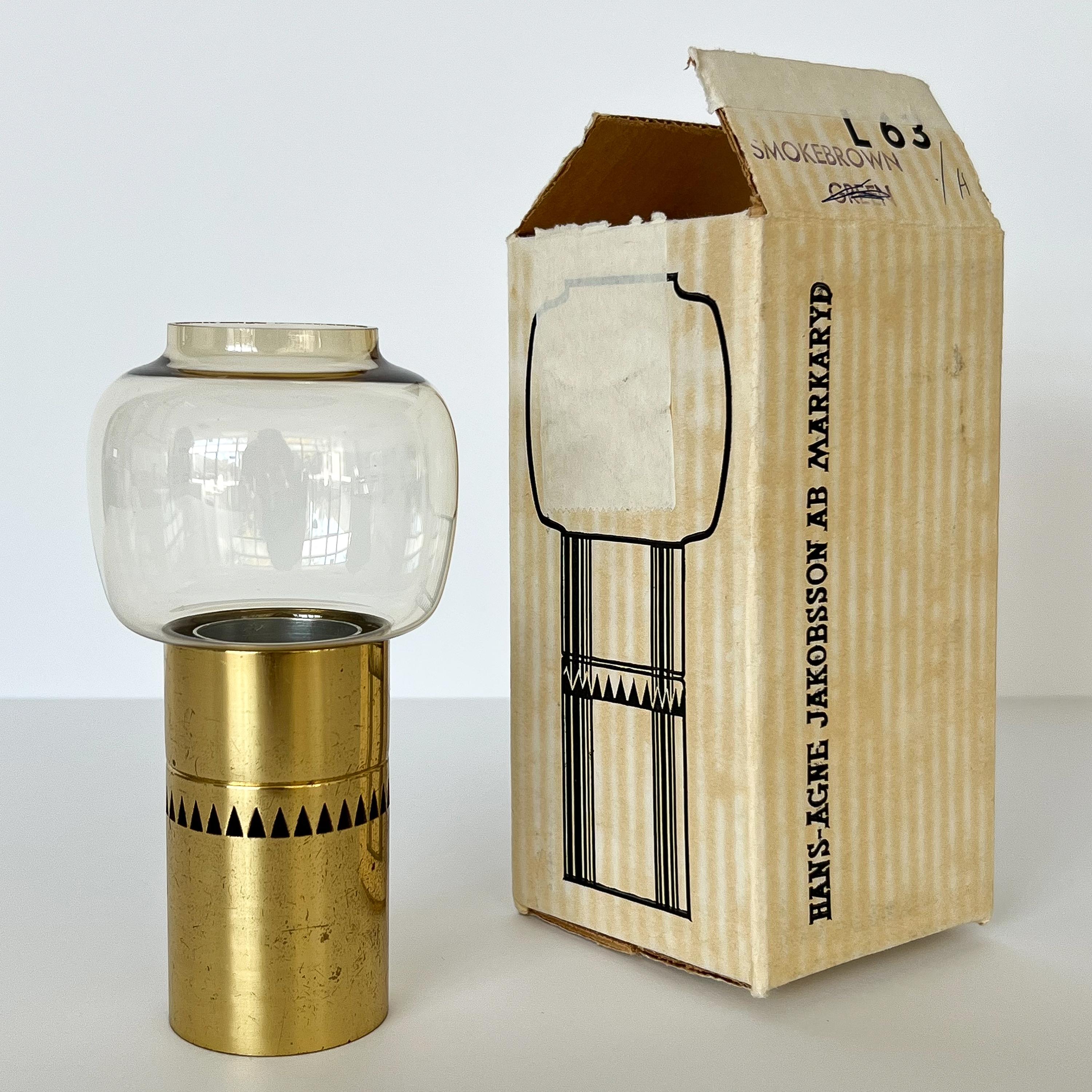 Hans-Agne Jakobsson brass and smoked glass hurricane candleholder for AB Markaryd, Sweden circa 1960s with the original box.  Model L63.  Brass cylinder base with stylized cut outs.  Base measures 3.5