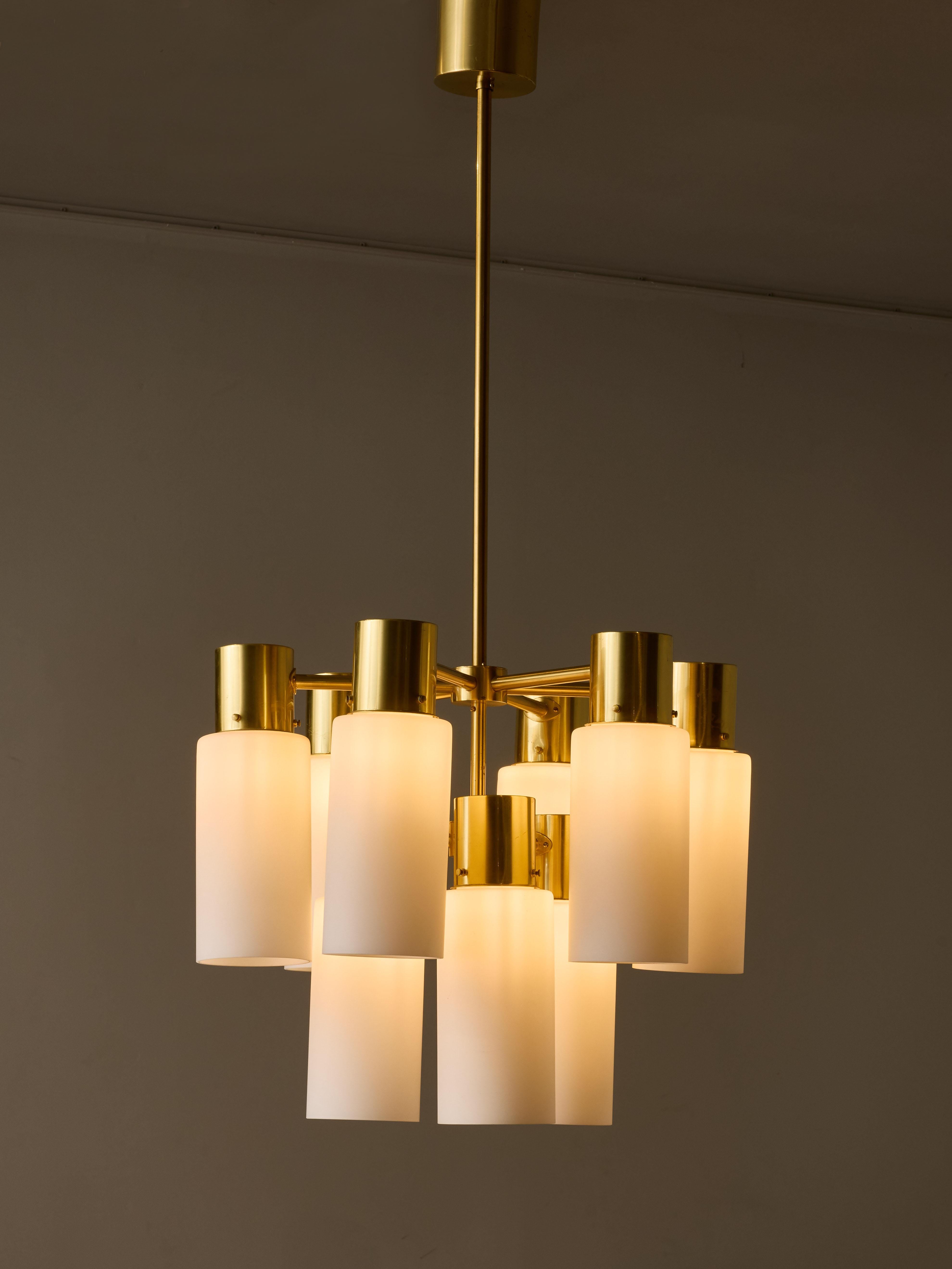 Due splendidi lampadari realizzati dal famoso designer svedese Hans-Agne Jakobsson, con finitura in ottone verniciato. Ogni lampadario vanta nove bracci di luce, progettati in modo elegante con paralumi cilindrici in vetro opalino rivolti verso il