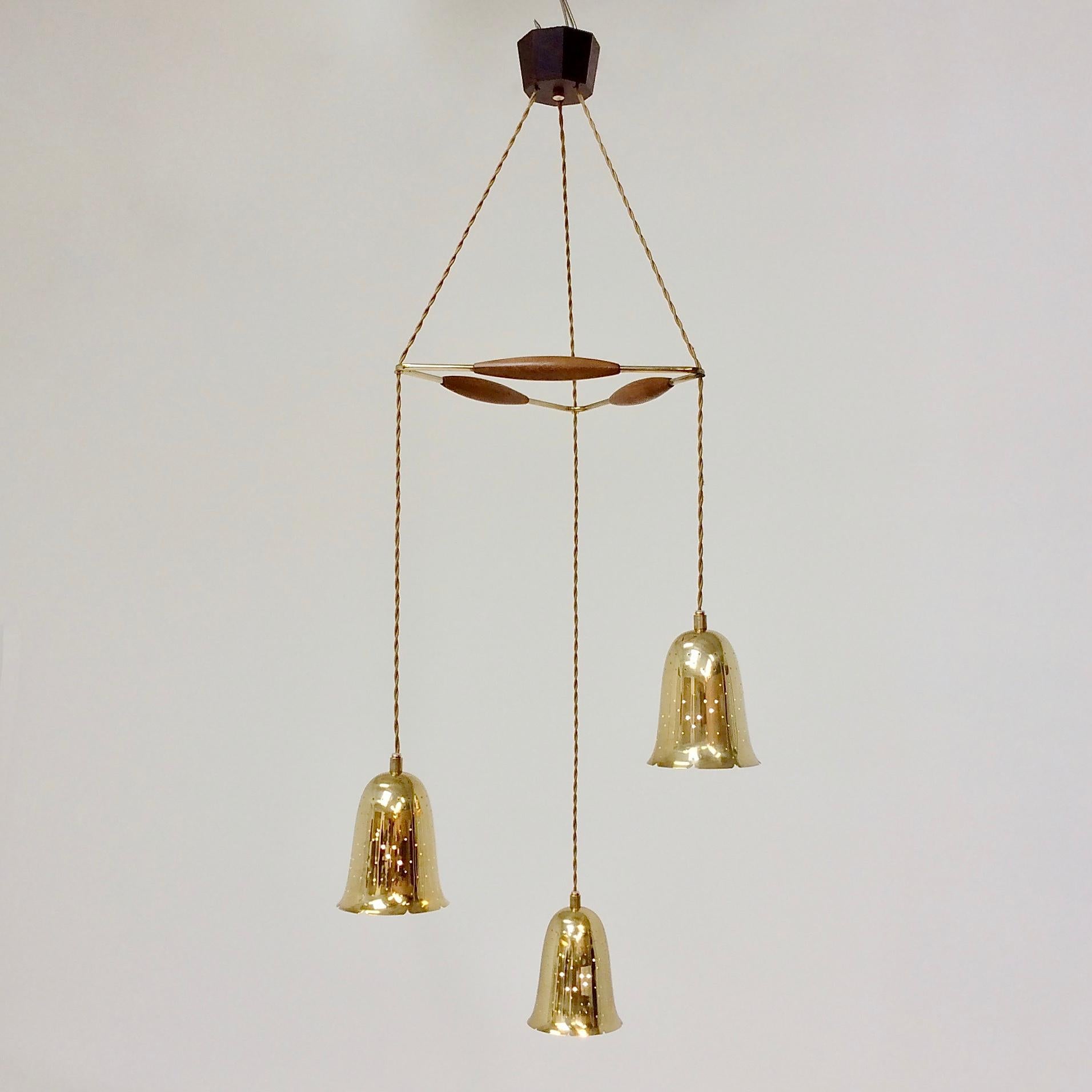 Elegant Hans-Agne Jakobsson pendant lamp, circa 1950, Sweden.
3 perforated brass shades, electric textile cords joined by a brass and solid wood triangle. Ceiling solid dark wood mount with brass detail.
3 little E 27 40W bulbs. Rewired.
Dimensions:
