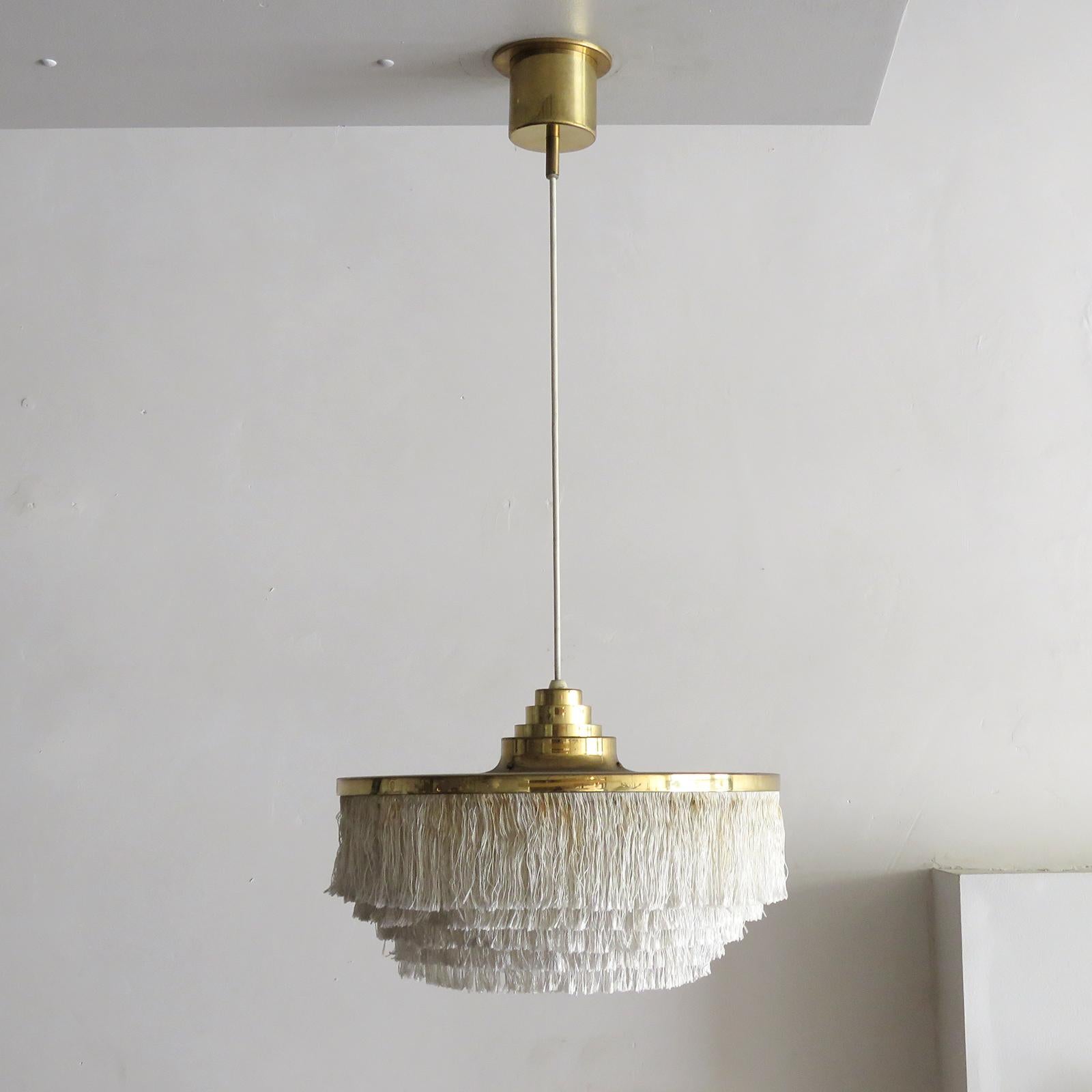 Wonderful pendant lamp by Hans-Agne Jakobsson for Markaryd, Sweden, 1960, with five tiers of off-white fringe silk cord with brass hardware frame and original brass canopy. Overall drop can be customized, wired for US standards, one E27 socket, max.