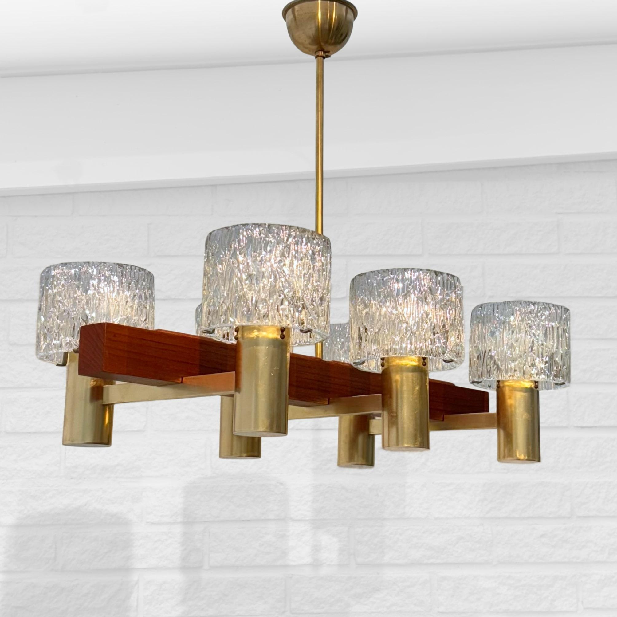 Un magnifique lustre scandinave du designer suédois Hans-Agne Jakobsson. Cette pièce exquise présente un corps en teck massif avec six élégants bras en laiton, chacun supportant un abat-jour en verre joliment moulé. Dotée d'une tige en laiton et