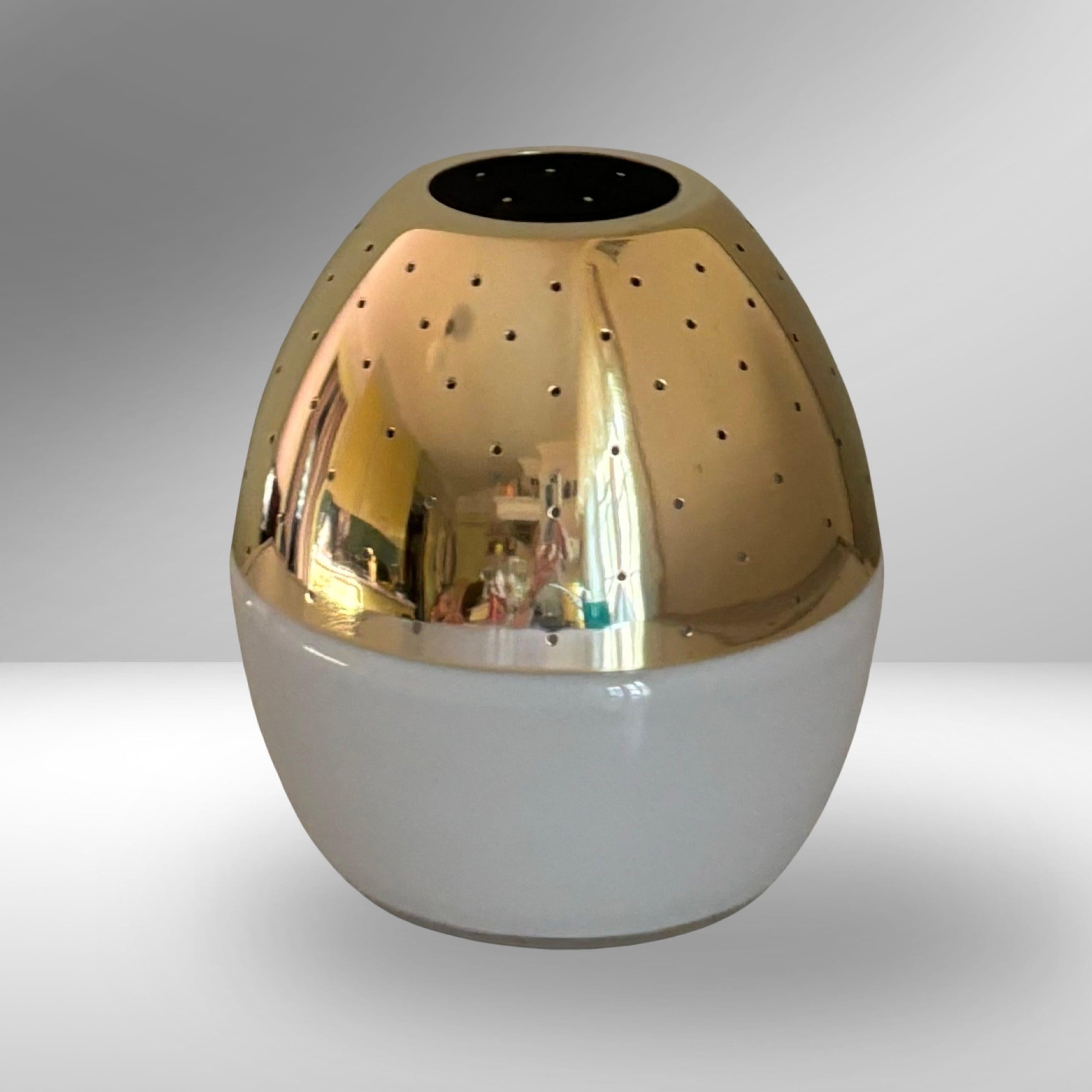 A minimalist egg-shaped candleholder model L163, produced by Hans-Agne Jakobsson in Sweden in the 1960s. It consists of a white opal glass base holding a dome-shaped top crafted from perforated brass. The small holes in the metal cast a decorative