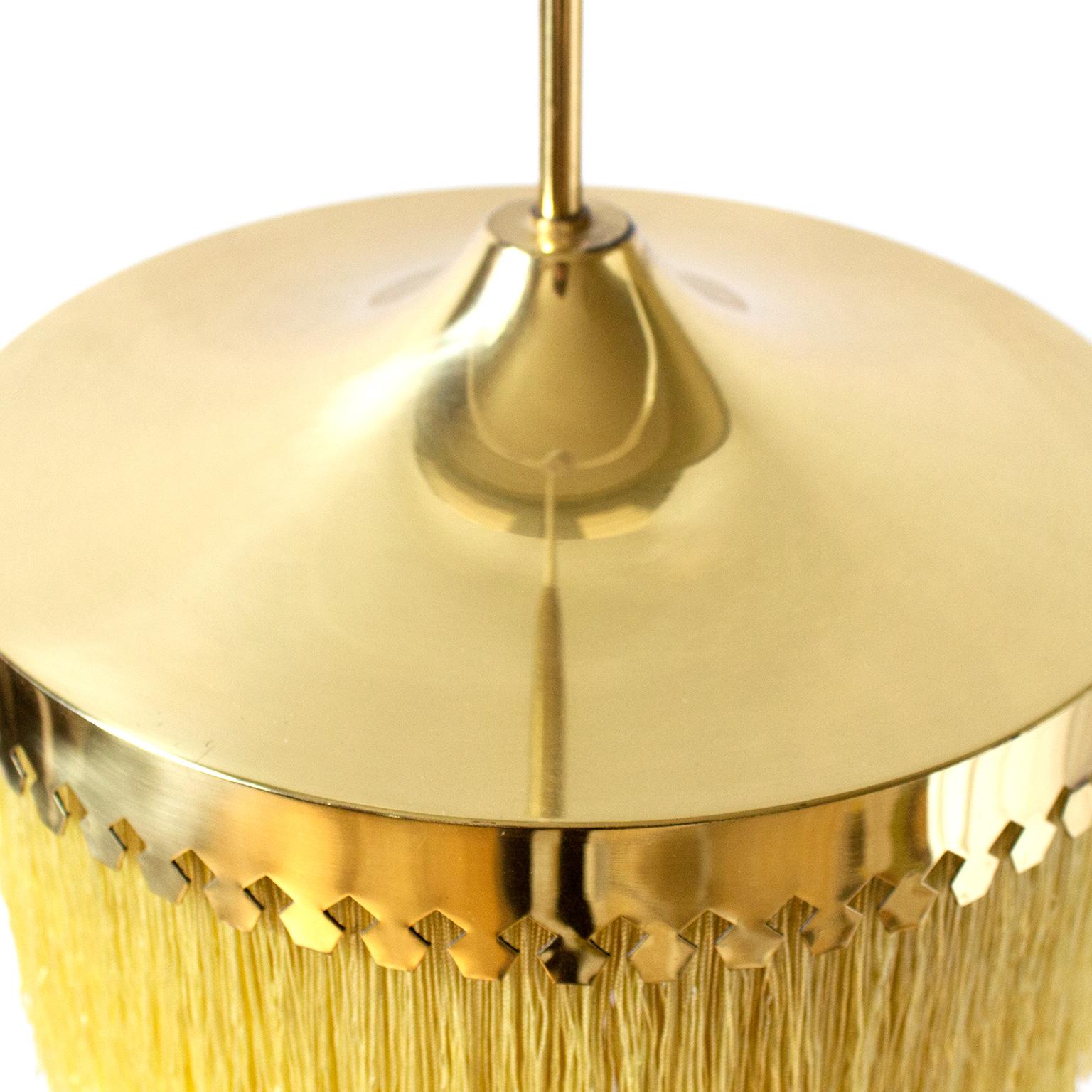 Swedish modernist Hans-Agne Jakobsson created this iconic pendant in 1960s with cut brass canopy with light yellow colored silk fringes. Wonderful condition and its original, still in line with age to both the brass and the silk. Fringe is a