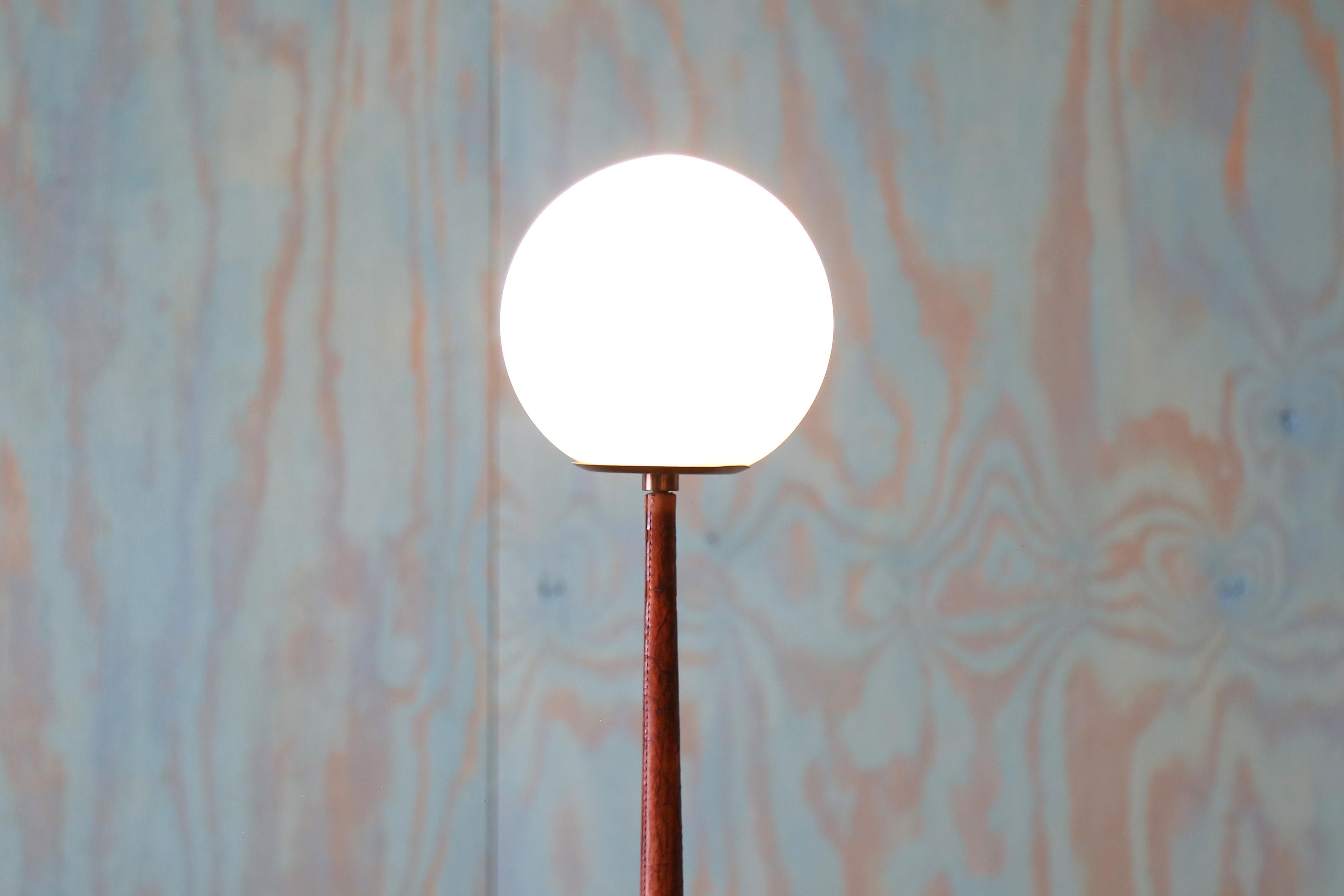 Cette lampe de table Hans Agnes Jakobsson pour Markaryd Sweden est rare. Elle est composée d'une base en laiton, d'une tige enveloppée de cuir cousu à la main et d'un globe en verre de lait sur le dessus.  Hans Agnes Jakobsson était connu pour sa