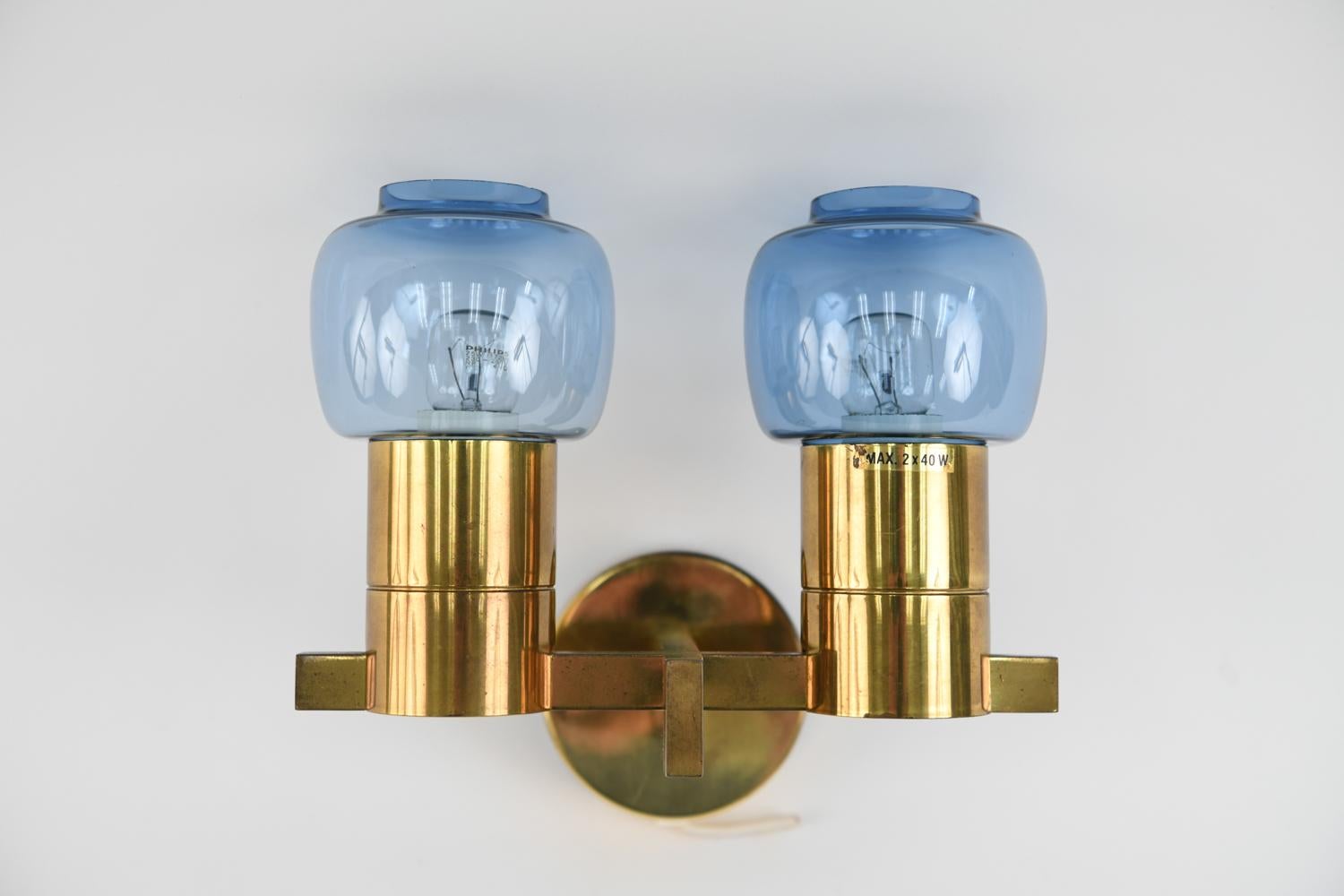 This double-arm sconce is model V-212 designed by Hans Agne Jakobsson. Featuring a brass base and glass globe shades, this Danish mid-century sconce is an attractive, iconic design.